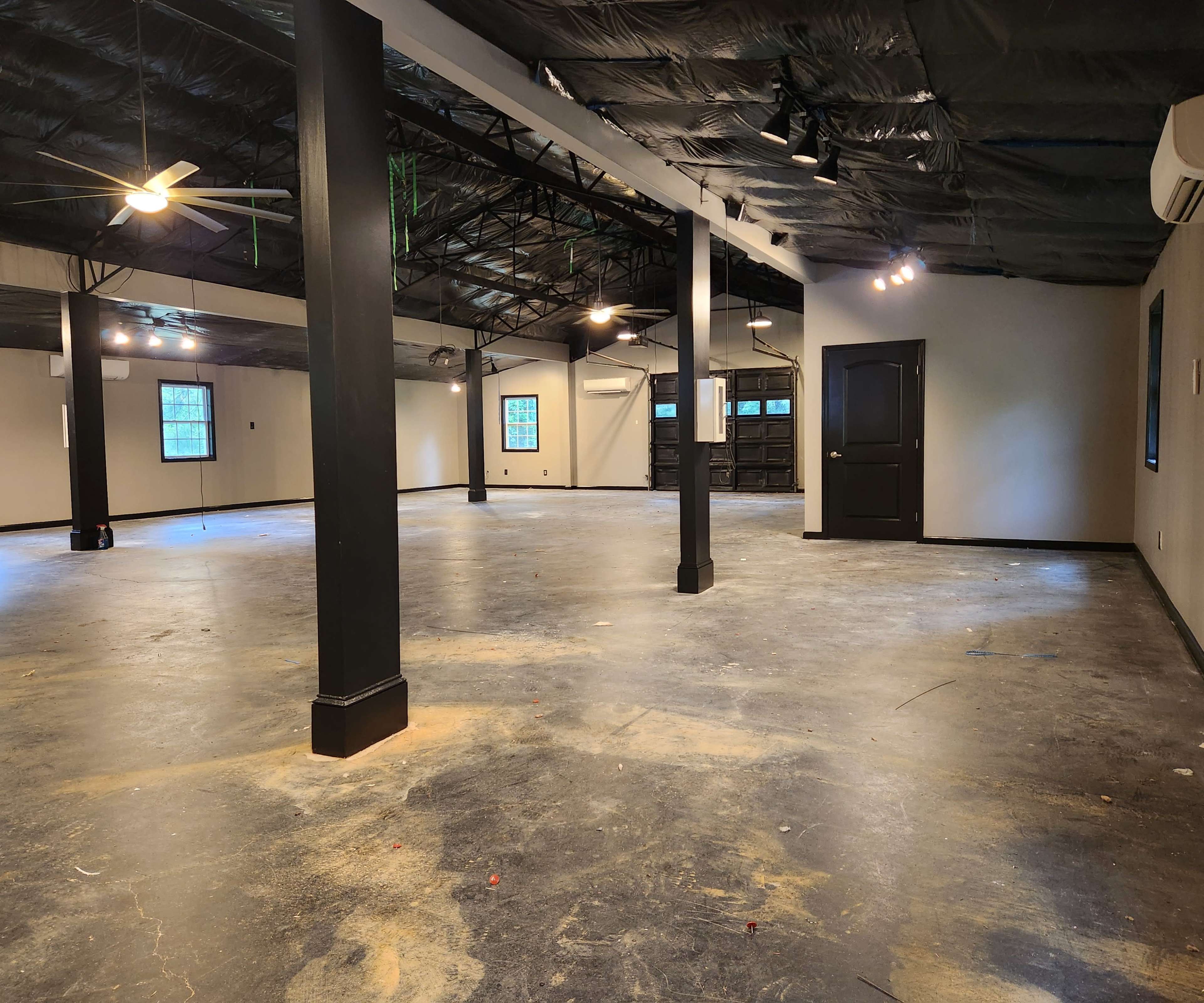 A large, empty room with a concrete floor, exposed beams, and multiple ceiling fans.