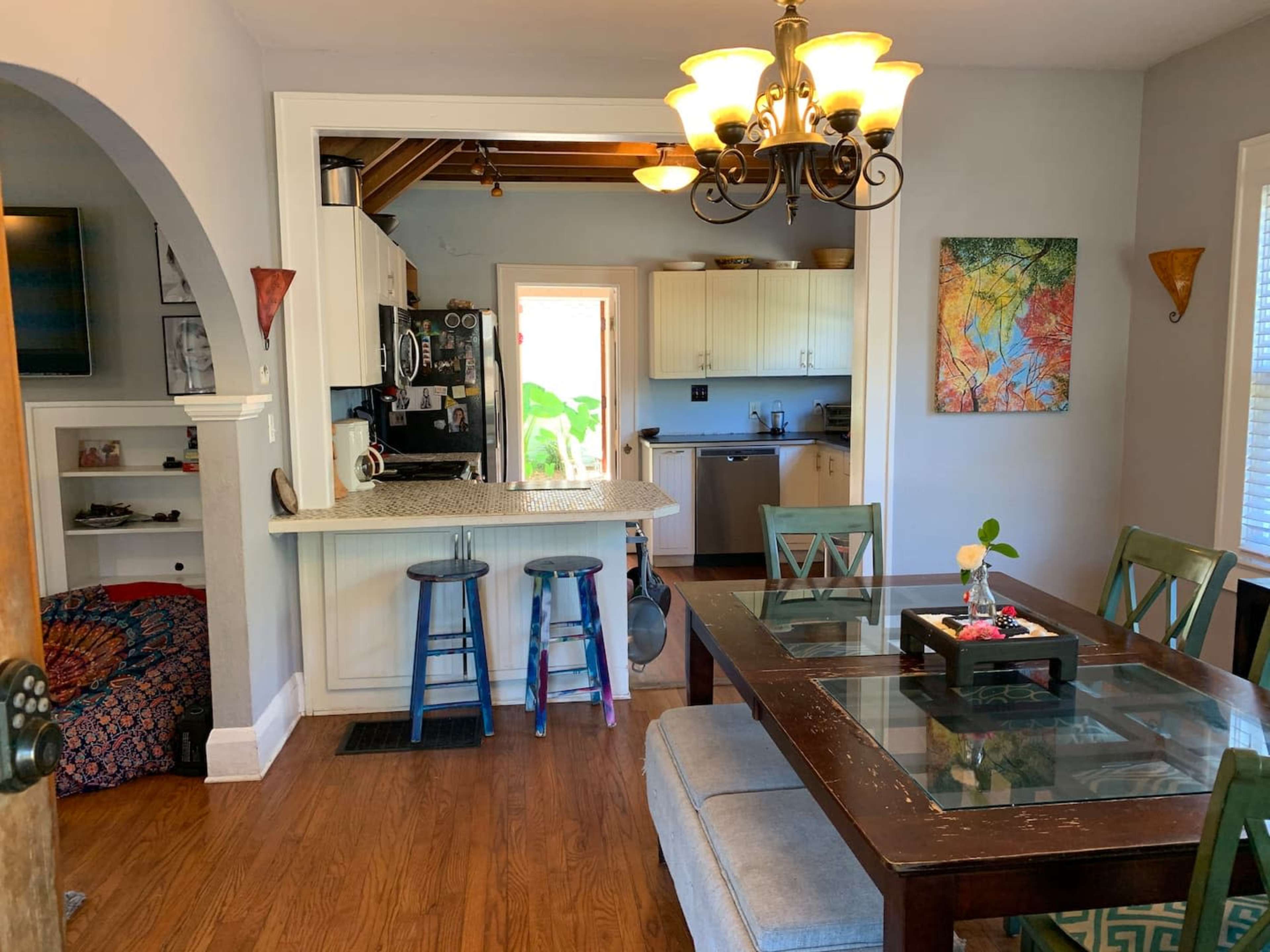 A dining area with a wooden table and chairs is positioned next to a kitchen with light-colored cabinets and a doorway leading outside.