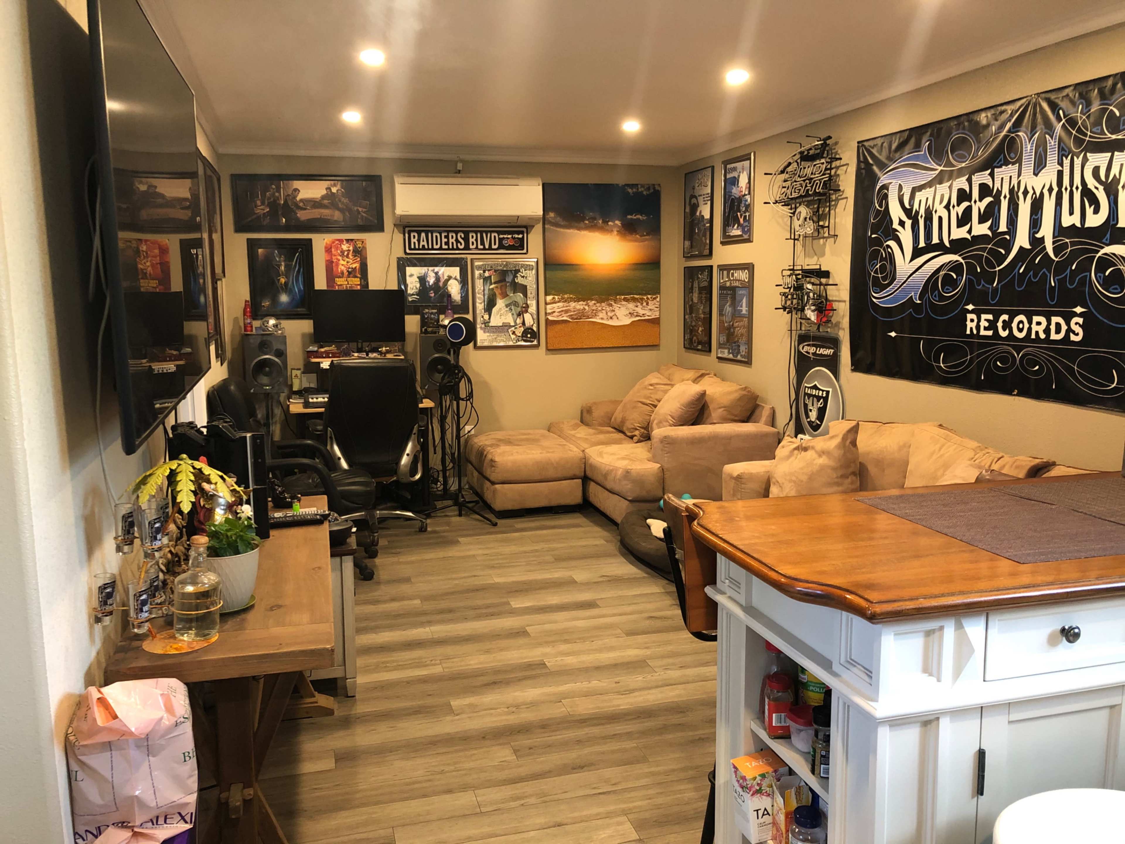 A room with beige couches, a small dining table, various framed posters on the walls, and audio equipment set up in the corner.