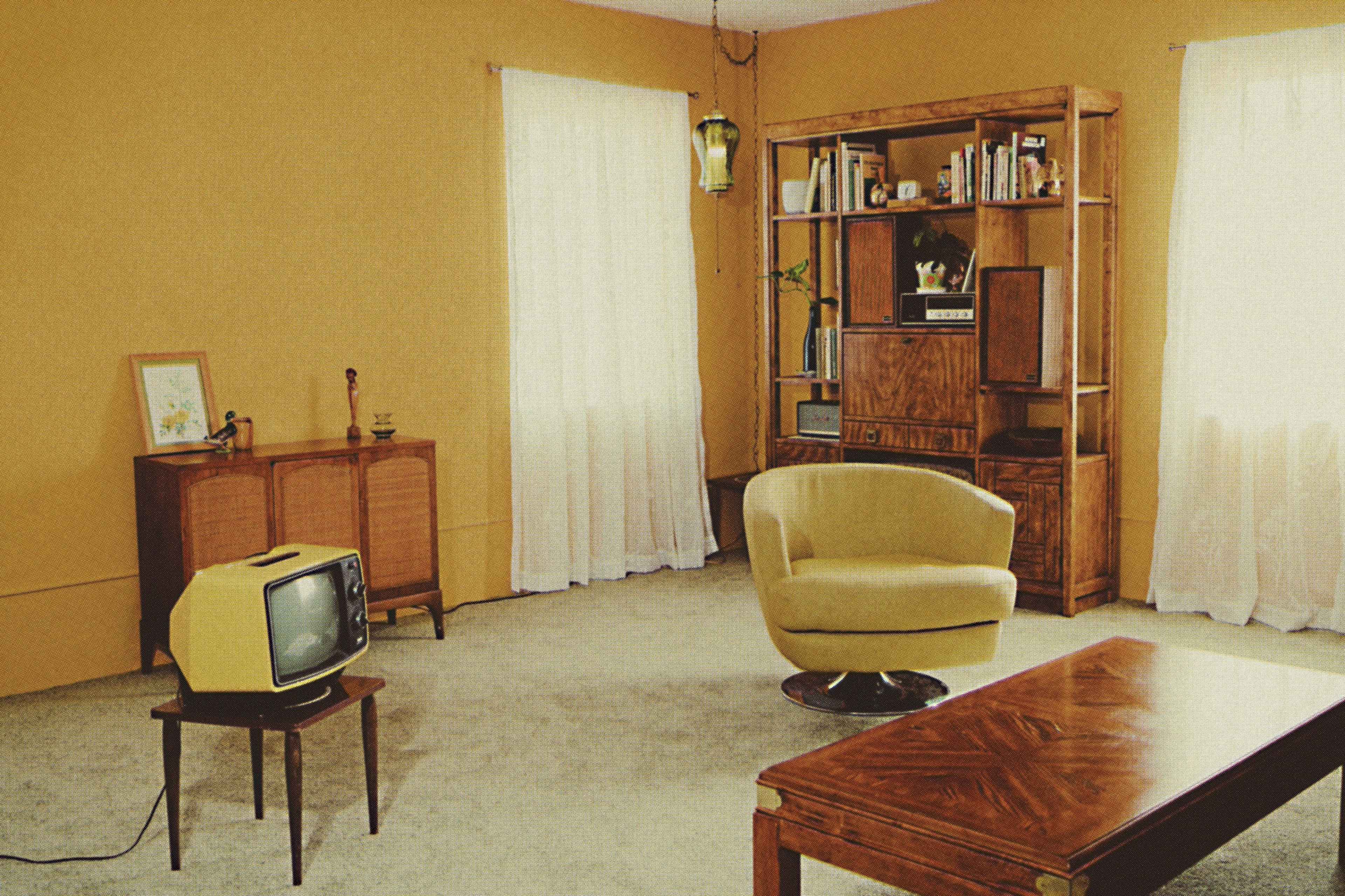 A mid-century living room with a yellow armchair, a vintage television on a small stand, and a wooden bookshelf filled with books.