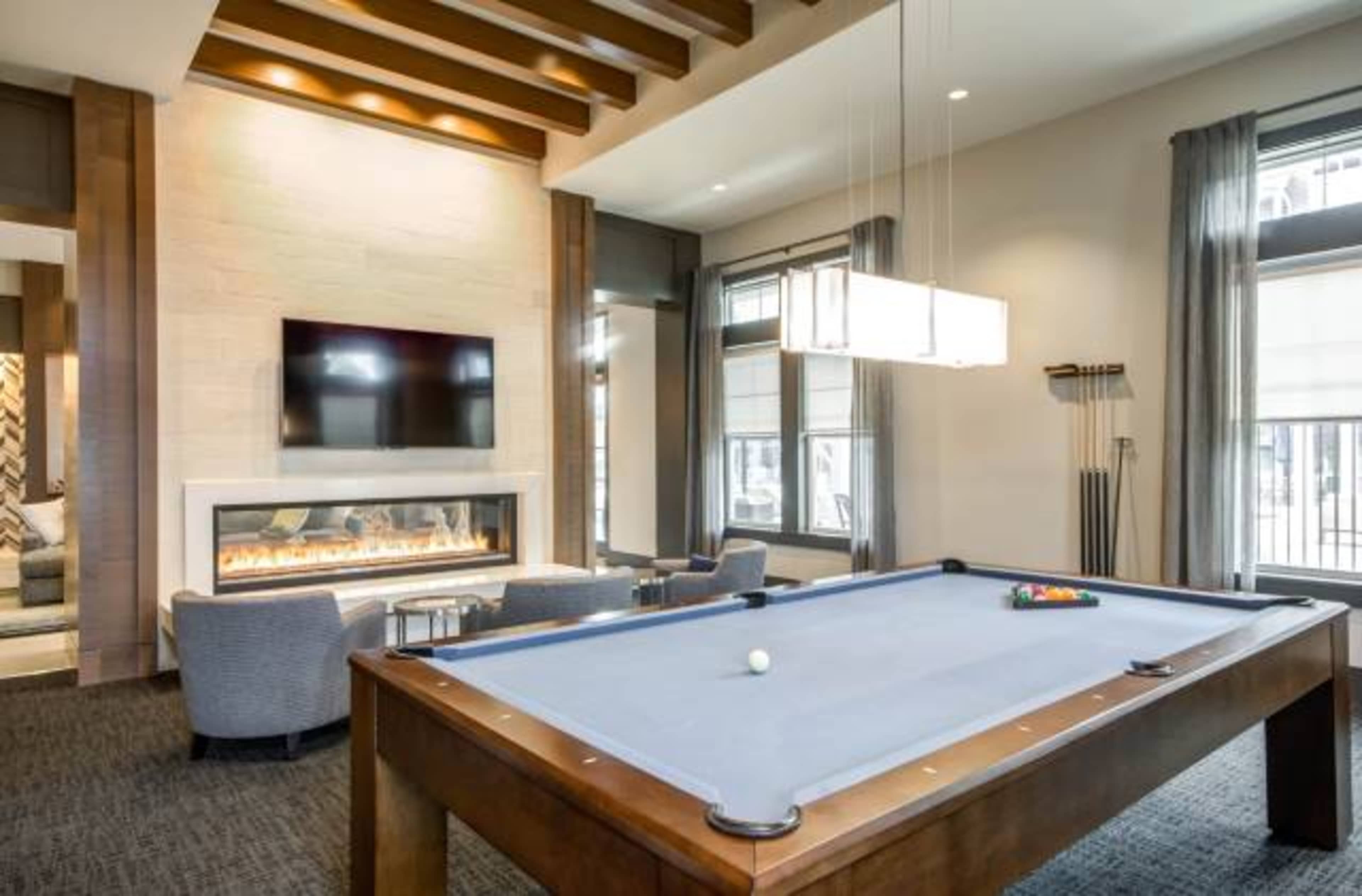 A modern room featuring a billiard table, a fireplace, and a television mounted on the wall.