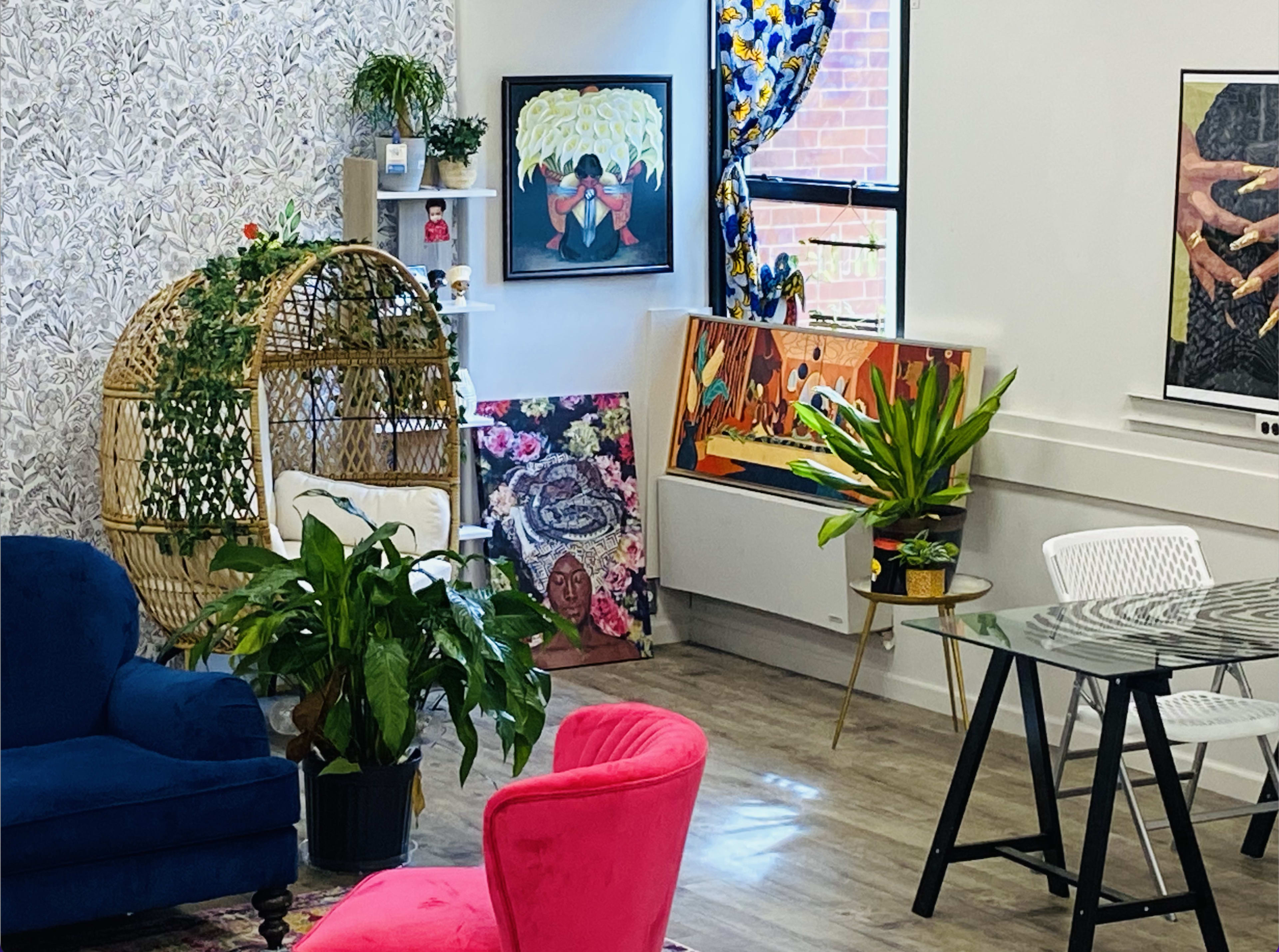 The scene features a modern interior with a blue couch, a pink chair, various plants, and colorful artwork displayed on the walls.