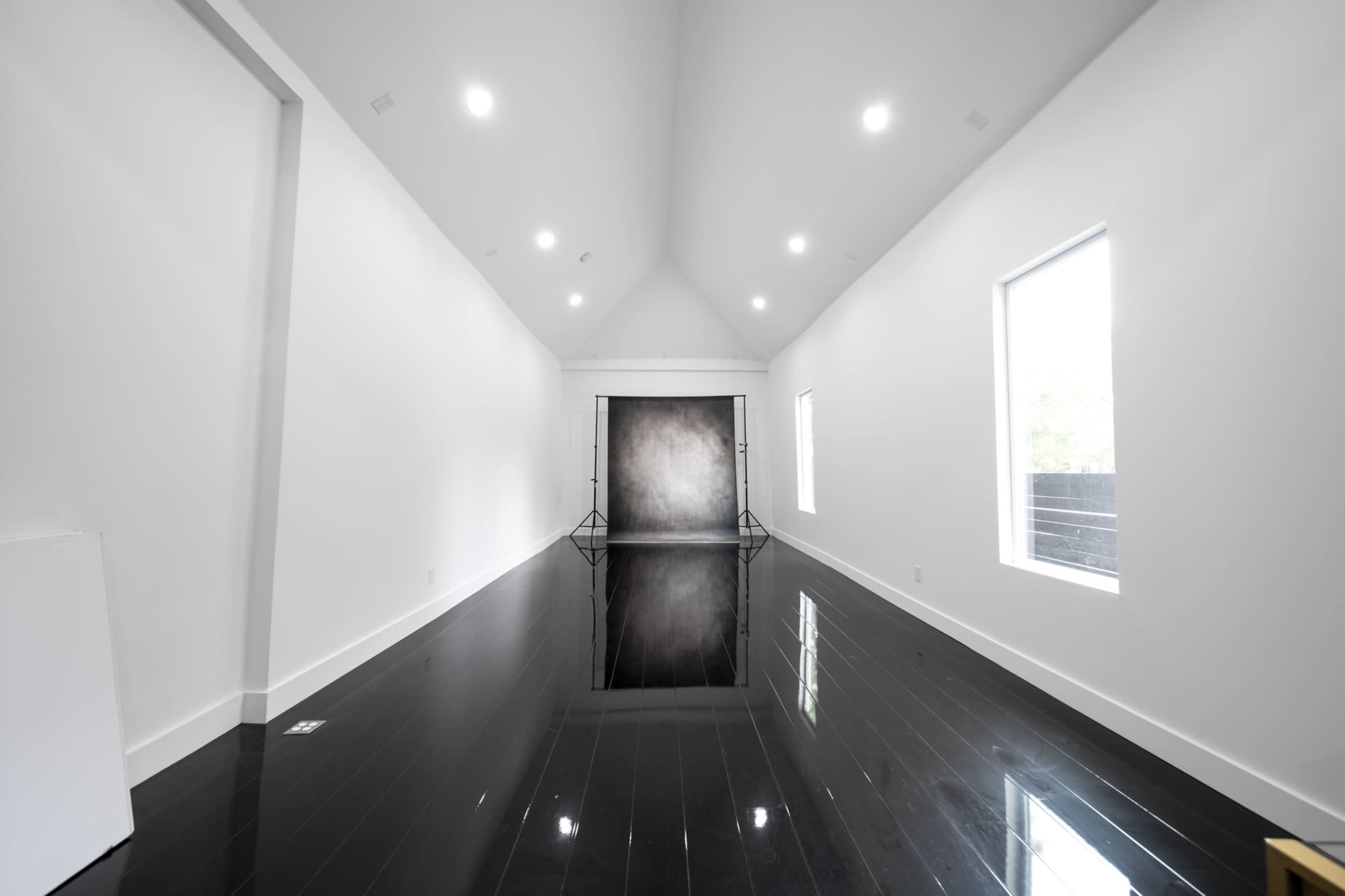 A spacious, modern room with white walls, large windows, and a reflective black floor.