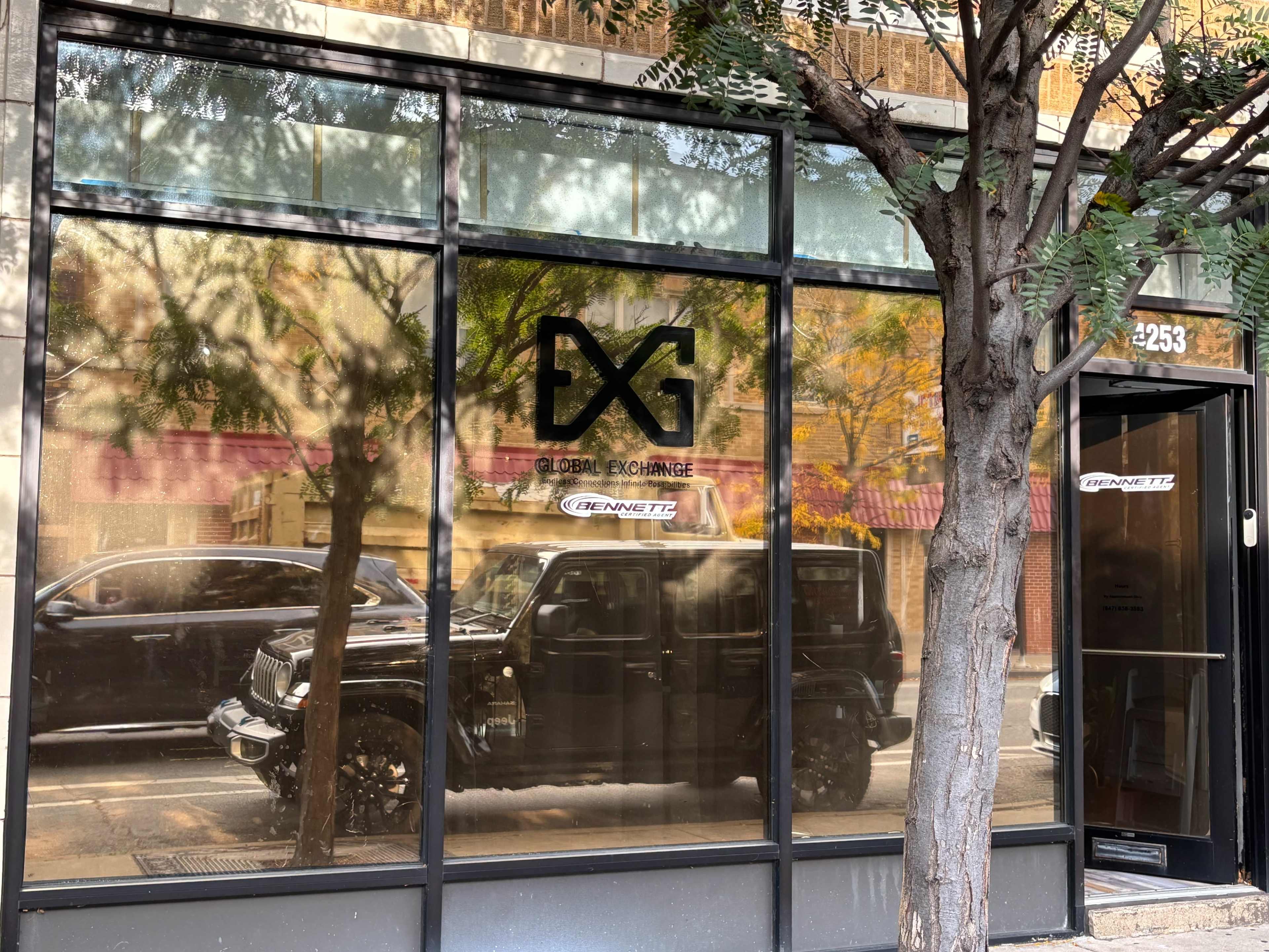 The image shows a storefront window with the text "GXG GLOBAL EXCHANGE" displayed, reflecting a street scene with a parked black vehicle and trees outside.