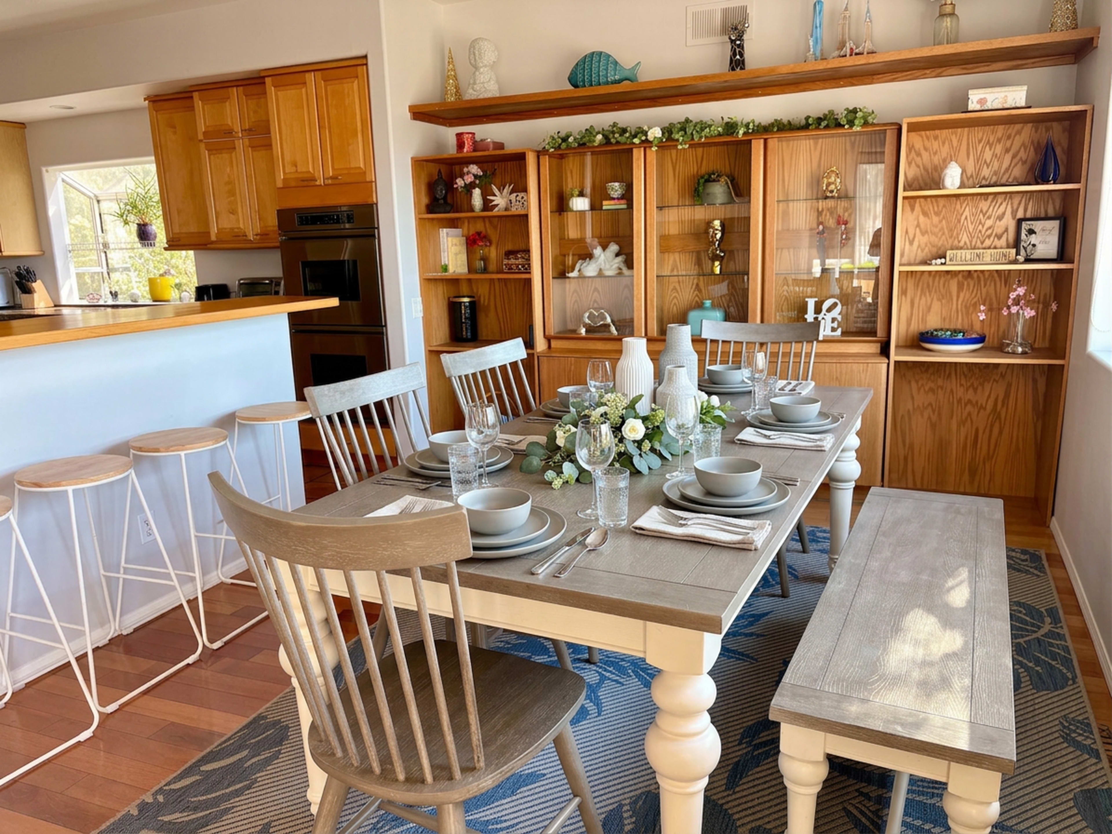A dining table is set with dishes and decorations in a well-lit room featuring wooden cabinetry and shelving.