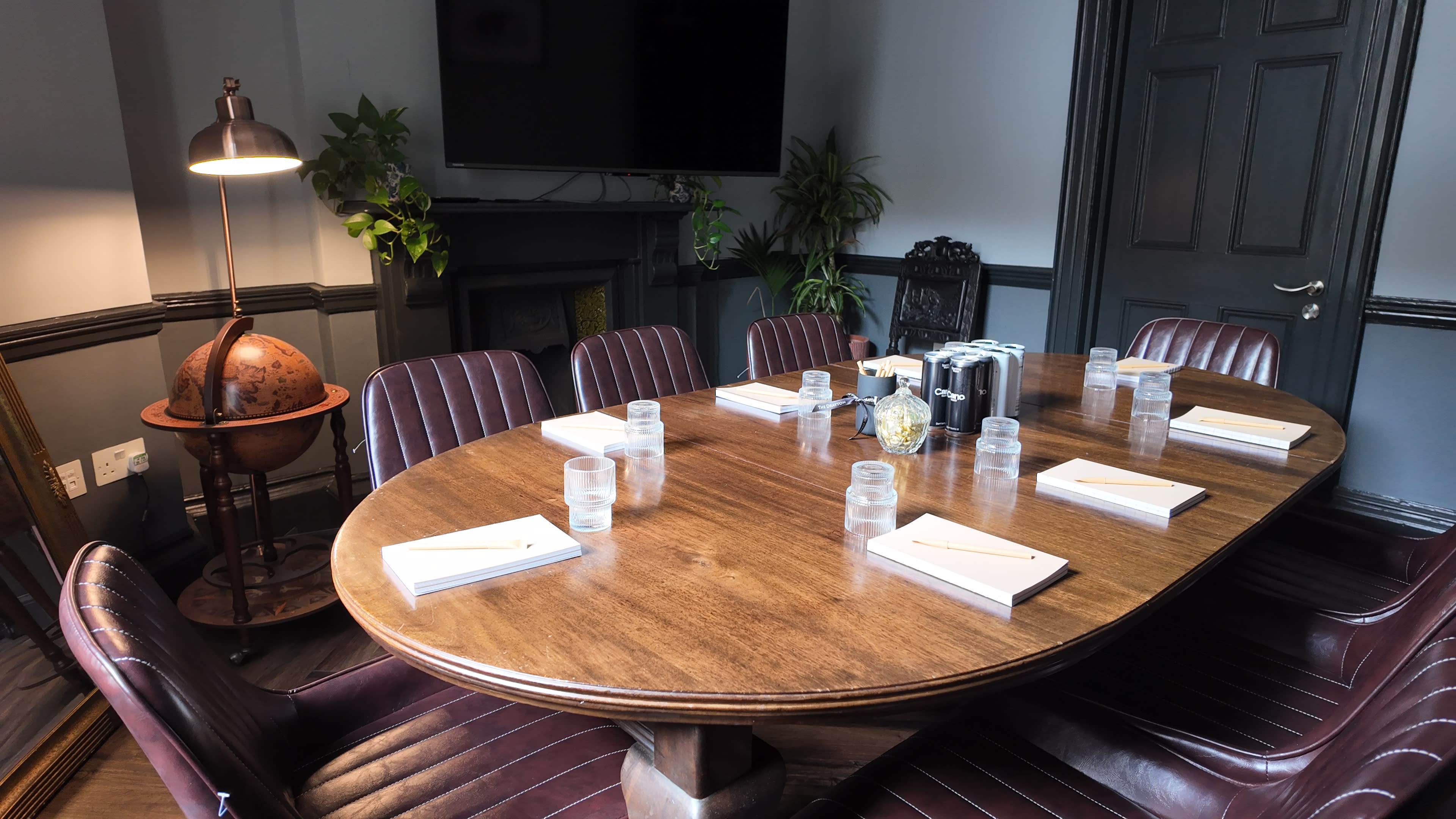 A large wooden table is set with notebooks and glasses of water, surrounded by leather chairs in a dimly lit conference room.