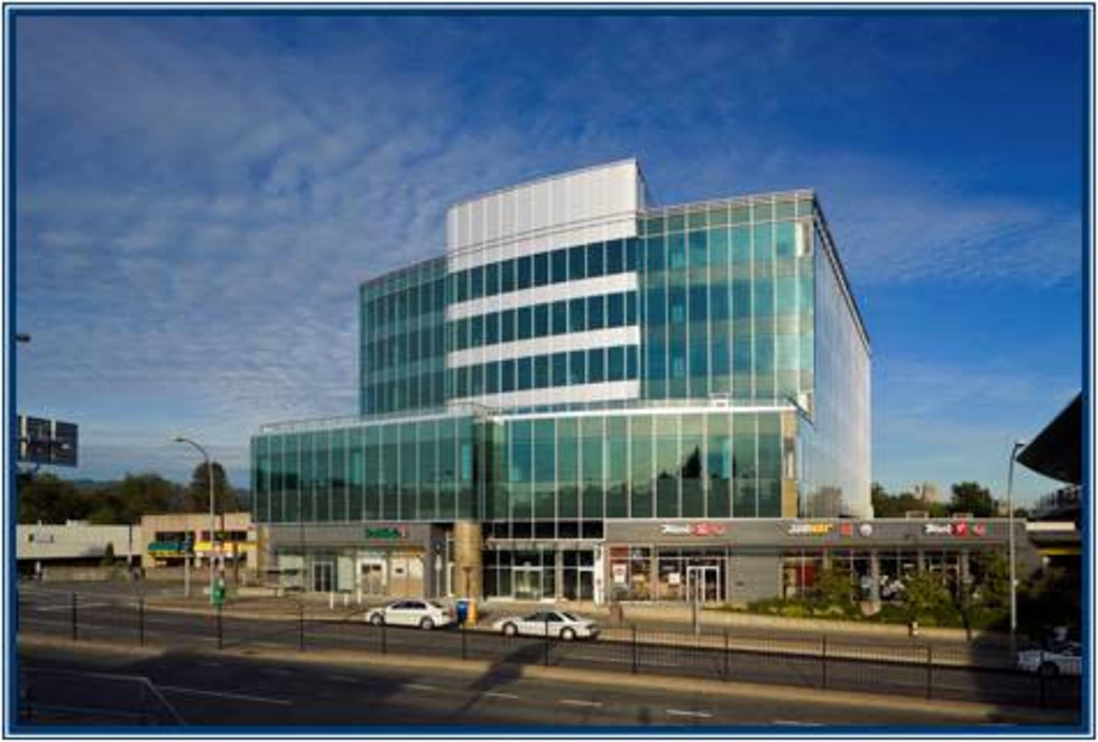 A modern glass-fronted office building stands at a busy intersection.