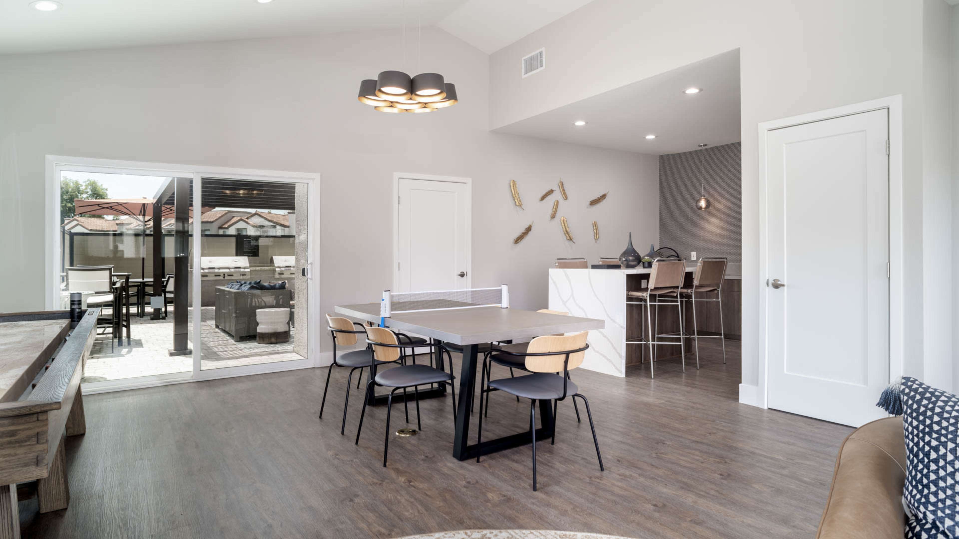 A modern dining area with a table and chairs, adjacent to an open kitchen and living space, featuring large sliding glass doors leading to an outdoor patio.