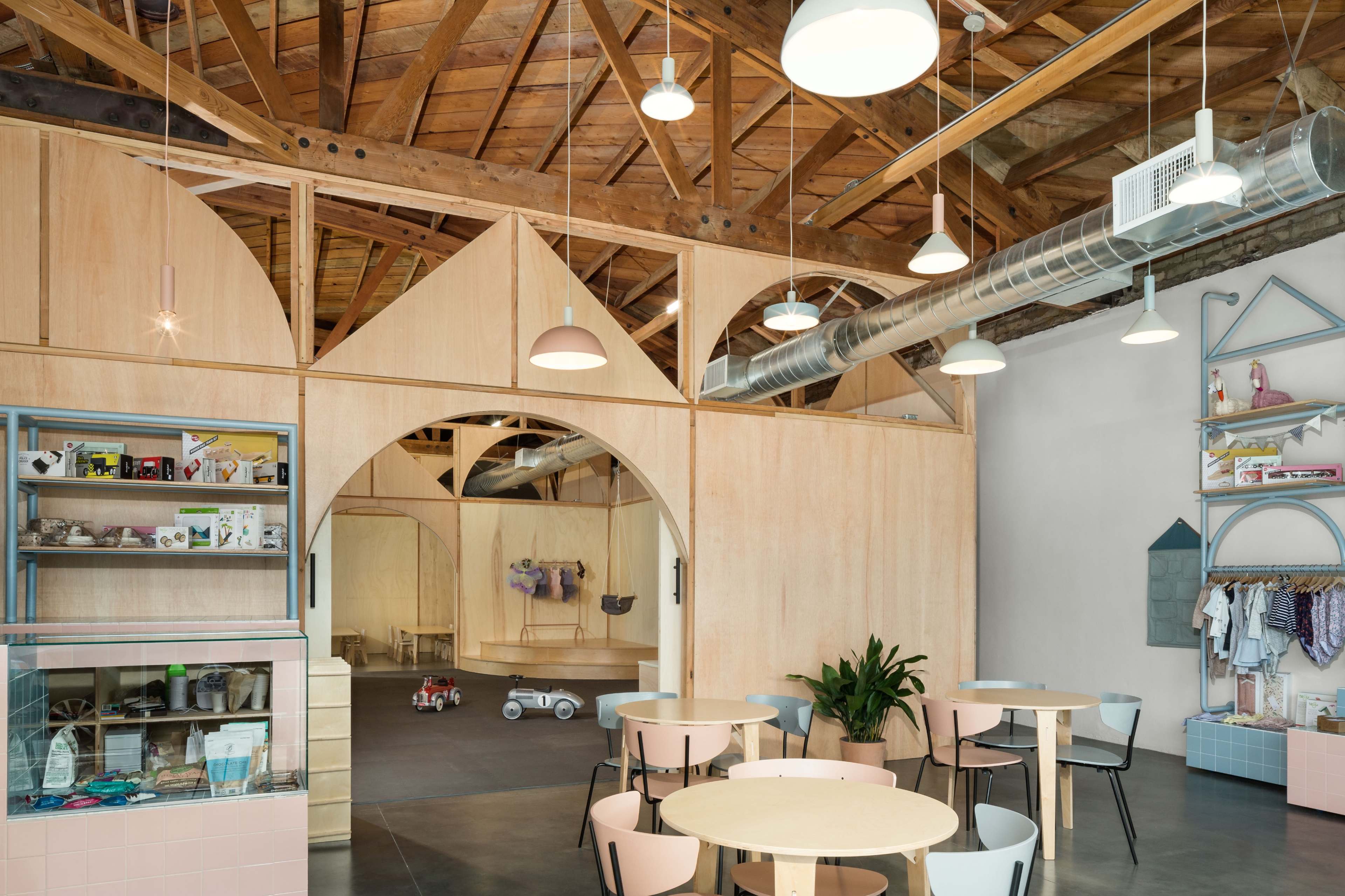 A modern interior of a café or retail space with wooden beams, light-colored walls, and a display shelf filled with products.