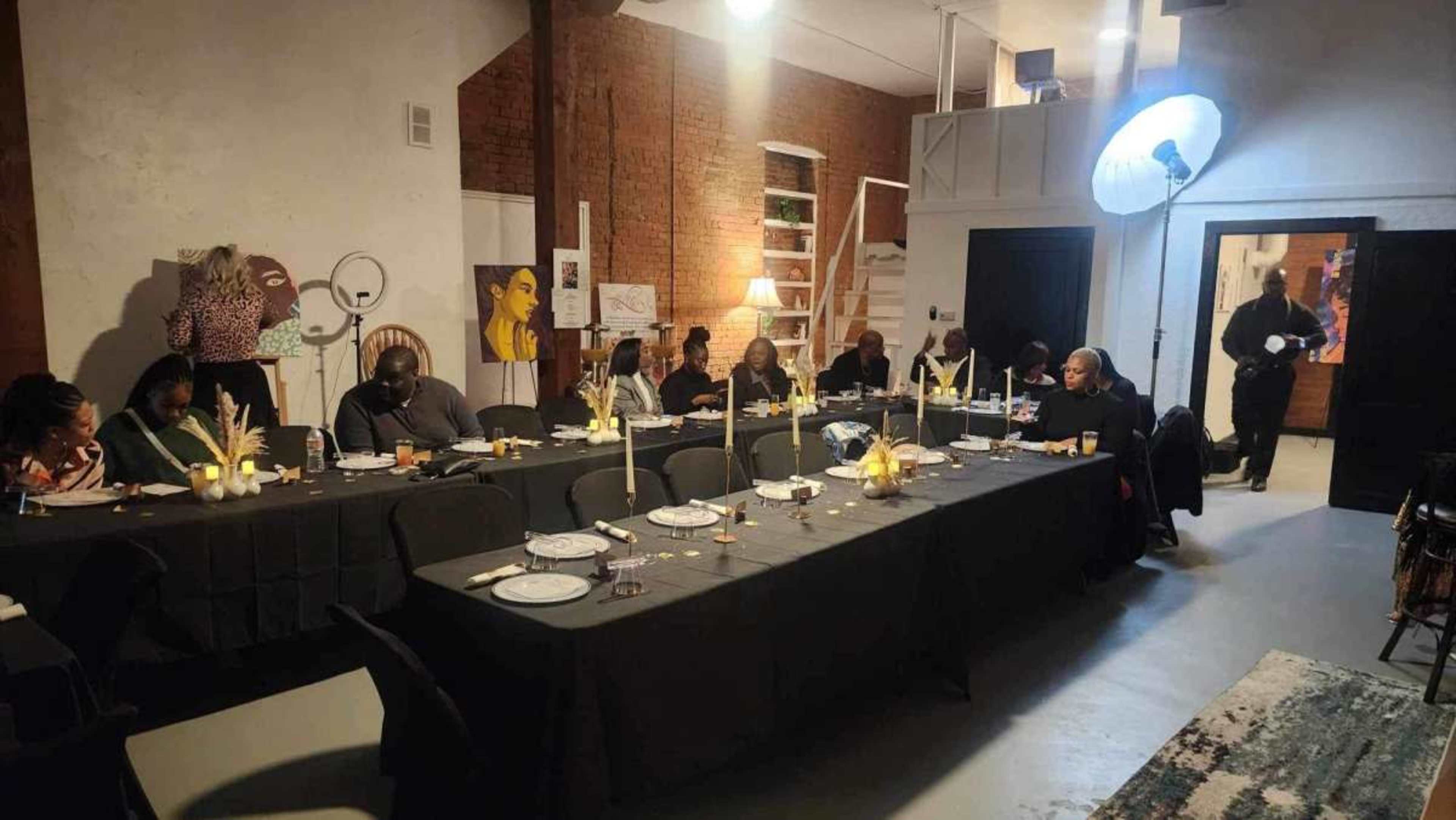 A long table is set for a formal dinner in a spacious room with exposed brick walls and stairs in the background.