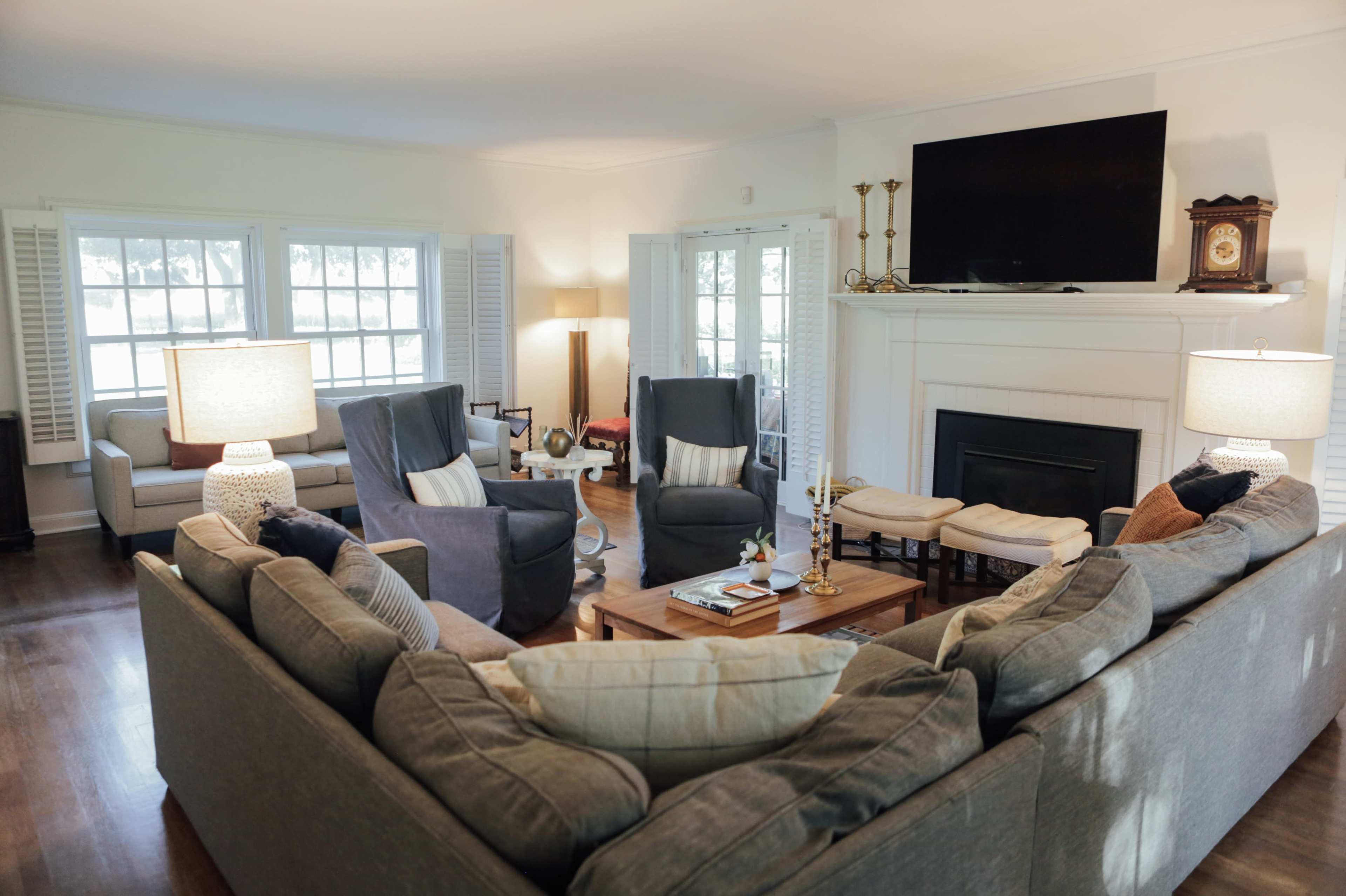 The living room features a sectional sofa arranged around a coffee table, with two armchairs and a television mounted above a fireplace.