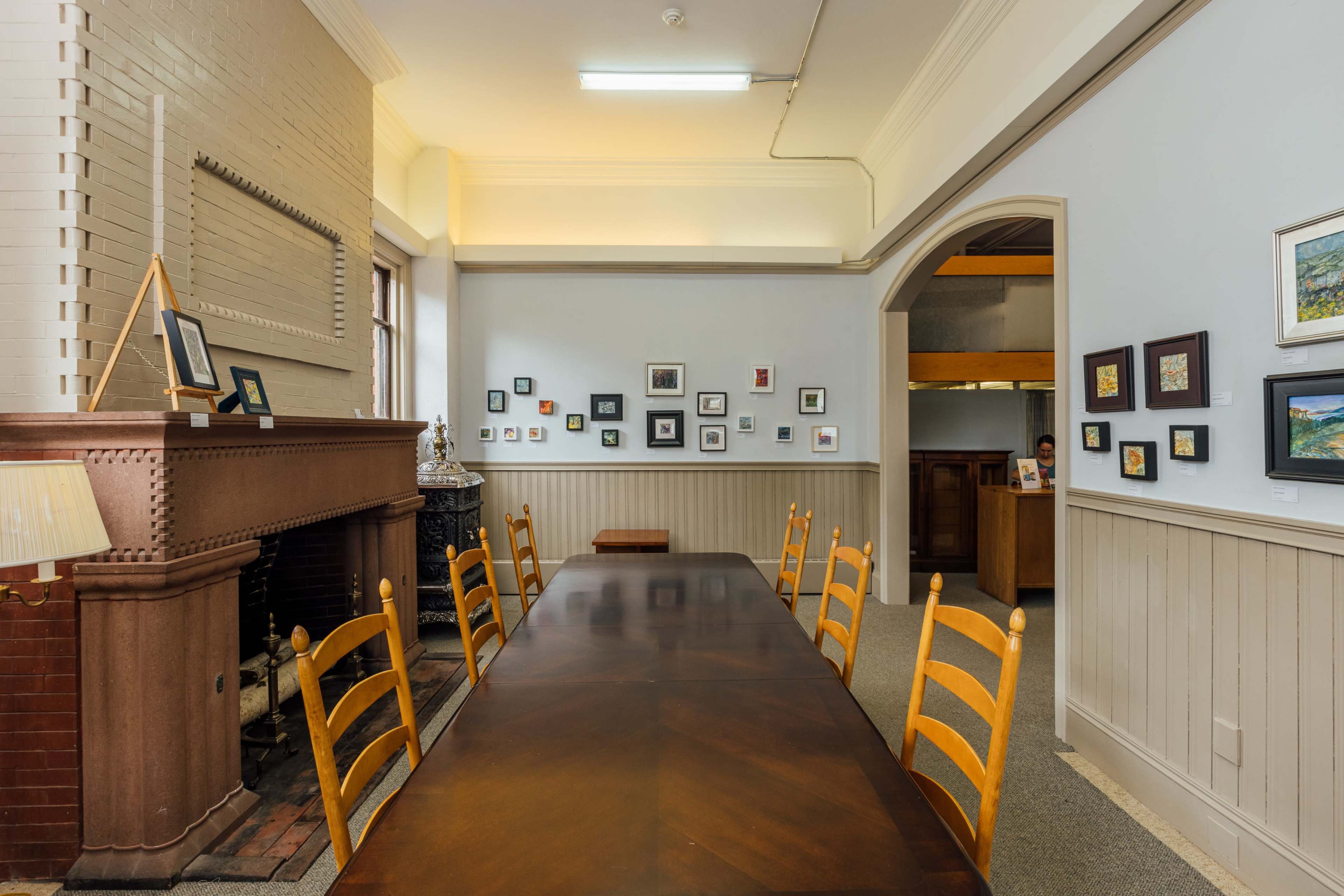 A long wooden table with chairs is set in a room featuring framed artwork on the walls and a brick fireplace.