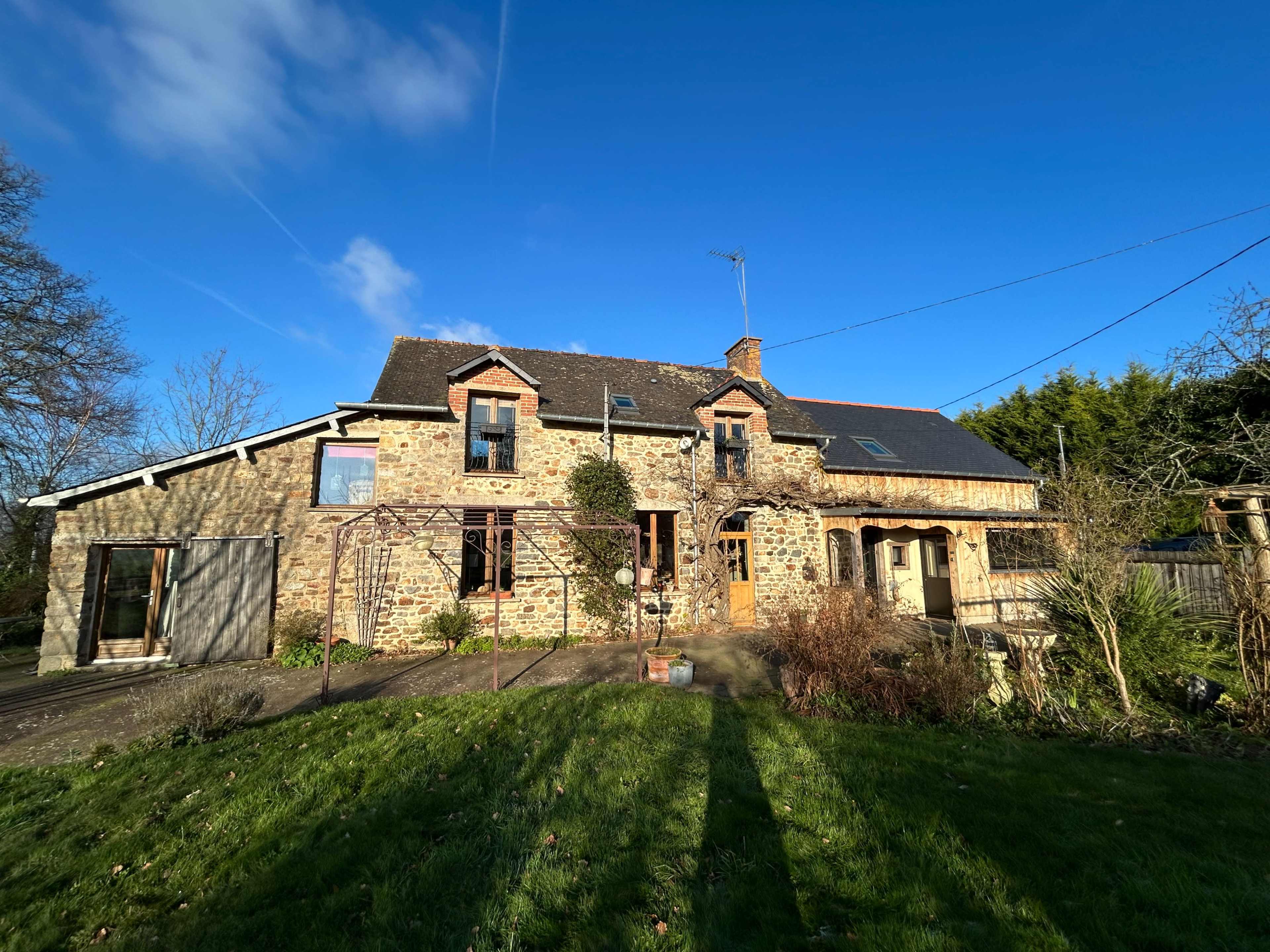 The image shows a large stone house with multiple gables, a well-maintained lawn, and a clear blue sky in the background.