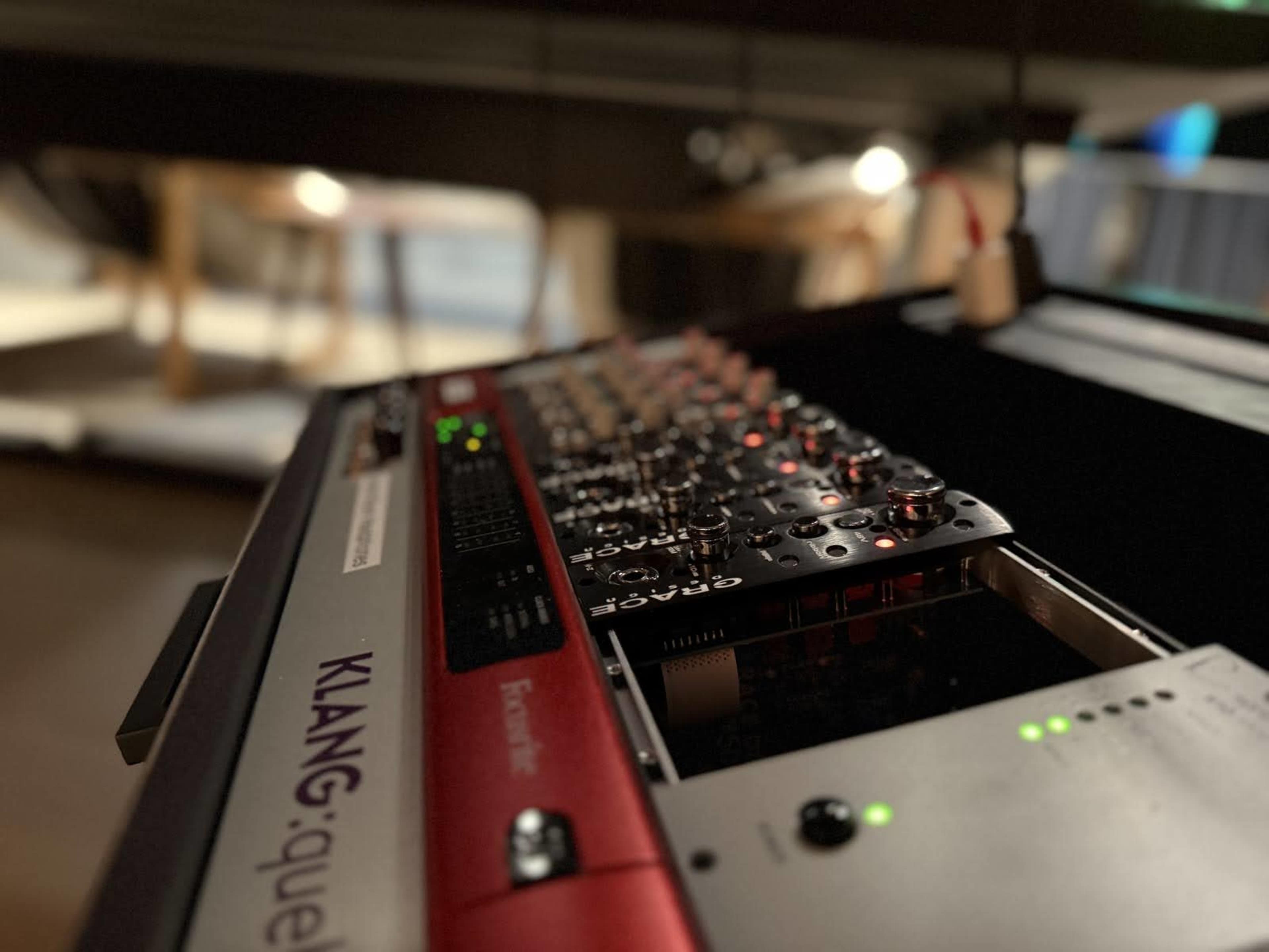 The image shows a close-up of a digital audio interface with knobs and lights, set against a blurred background of a studio environment.