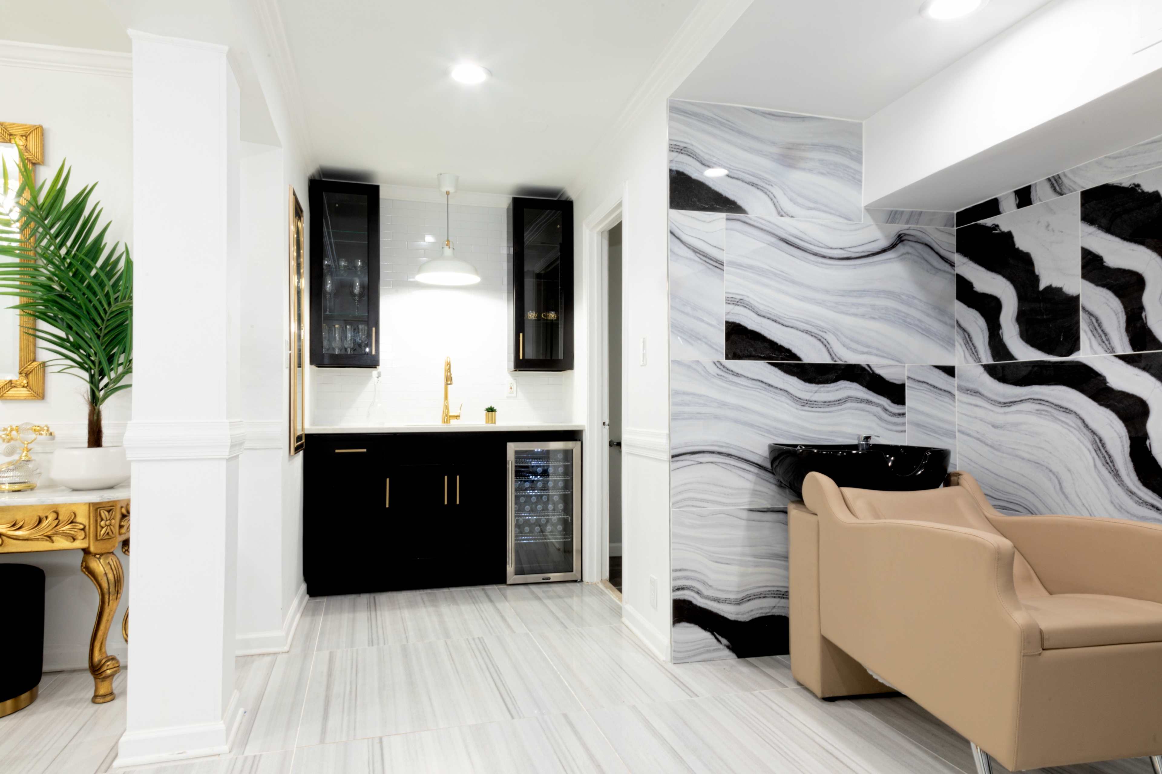 A modern interior featuring a black and white marble wall, a small kitchenette with dark cabinetry, and a beige armchair.