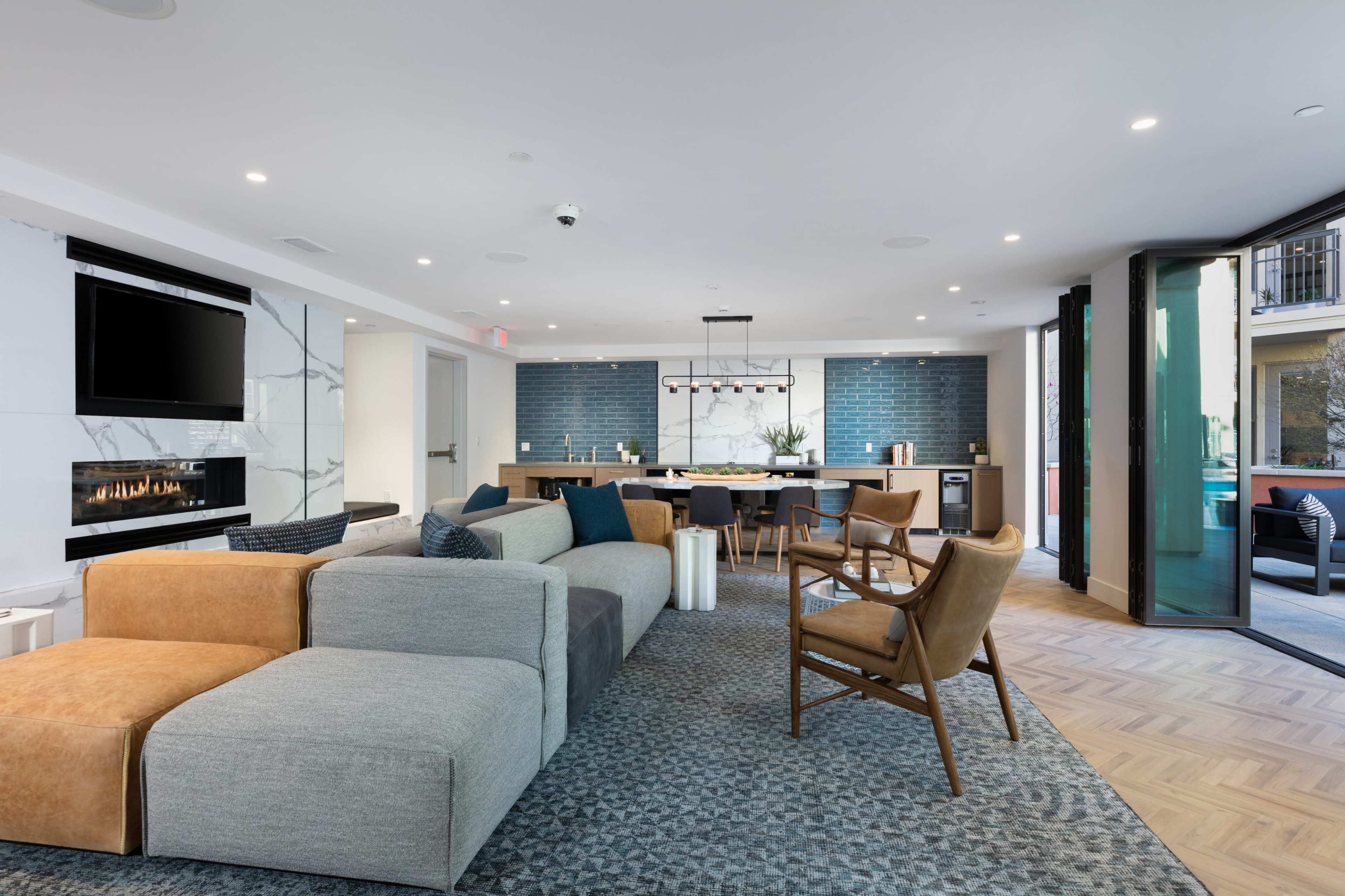A modern lounge area featuring a sectional sofa, an armchair, a fireplace, and a kitchen bar with seating.