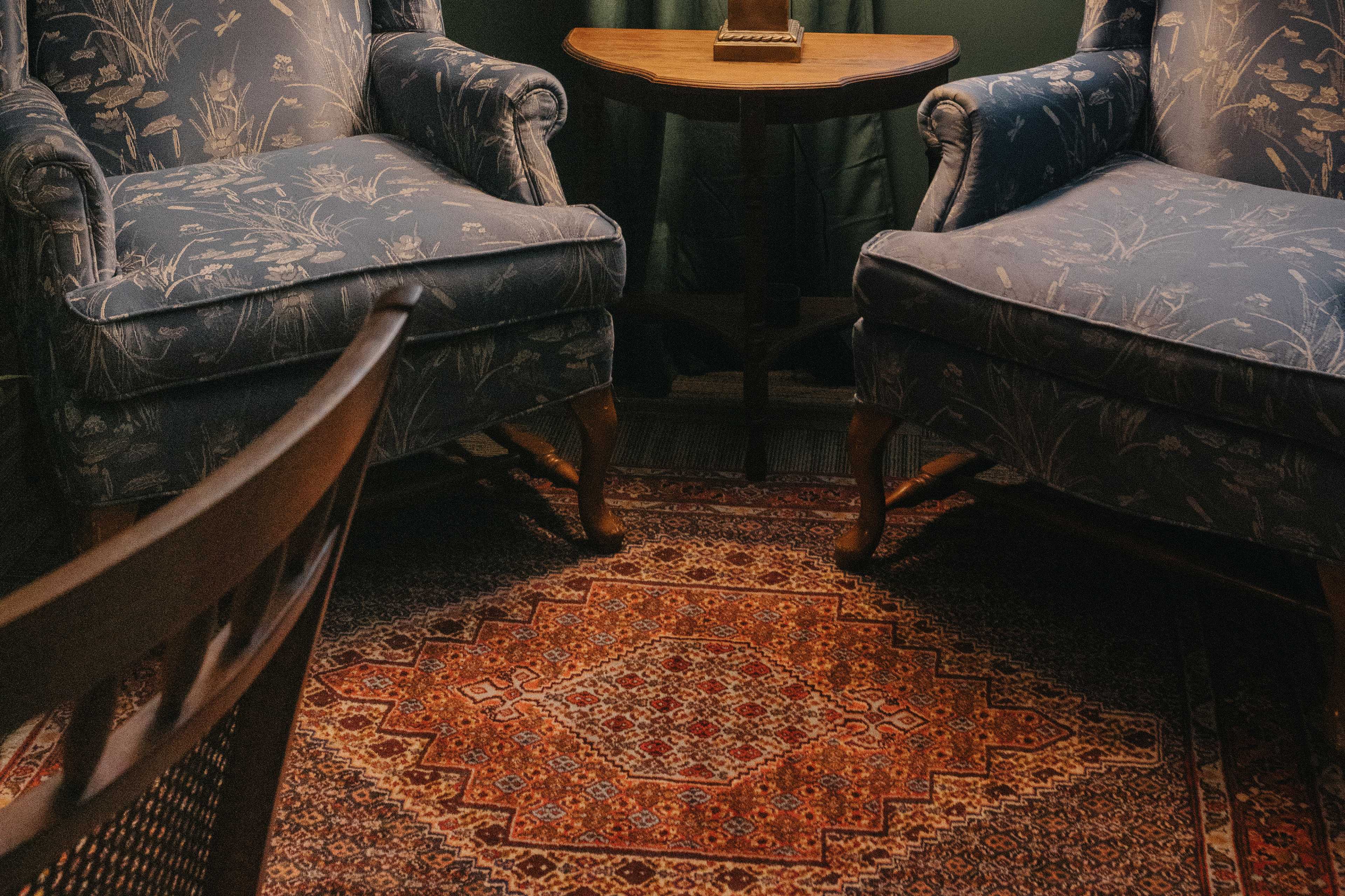 Two upholstered chairs facing each other over an intricately patterned rug, with a small wooden table between them.