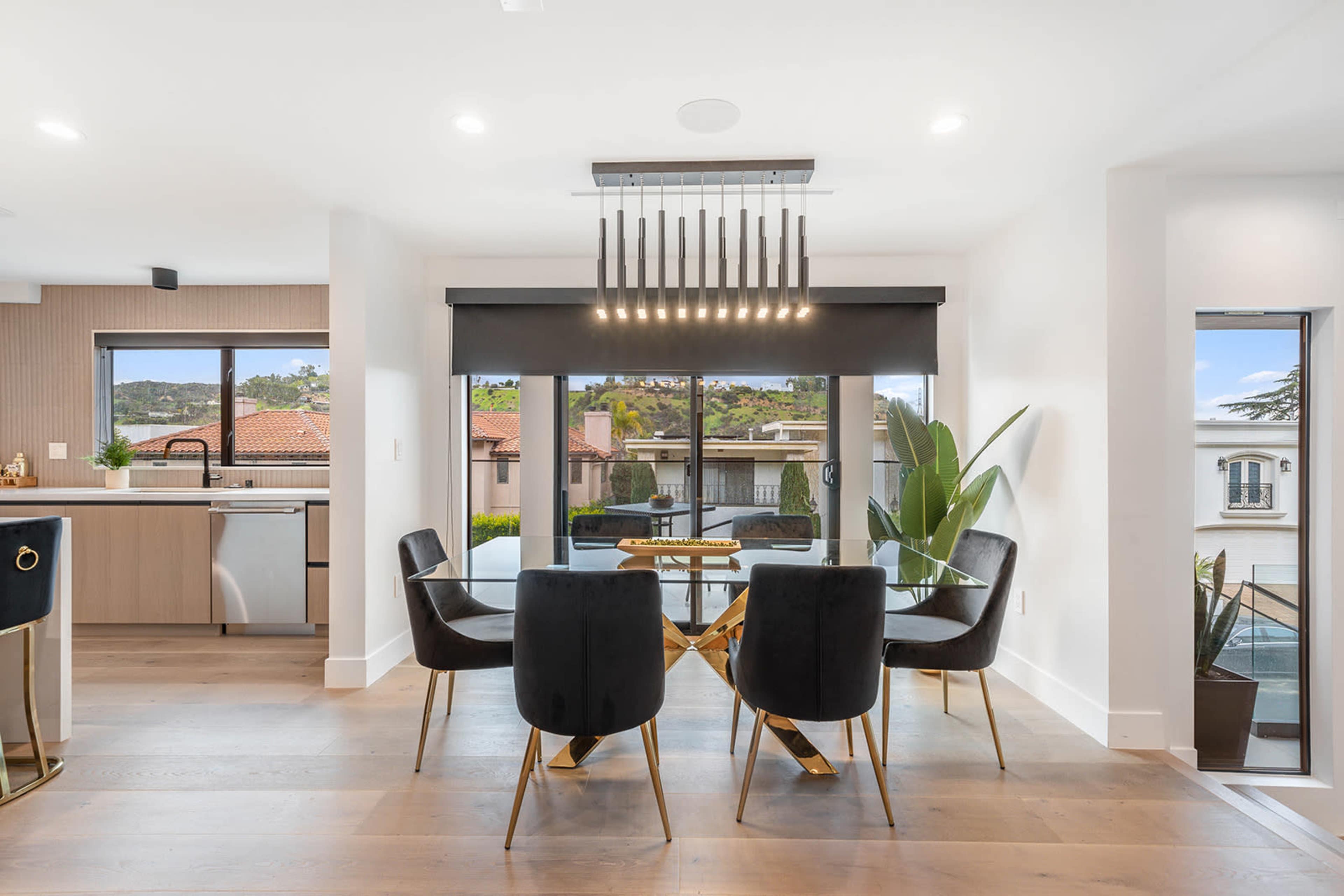 A dining area features a round glass table surrounded by black upholstered chairs, with large windows offering views of a scenic exterior.