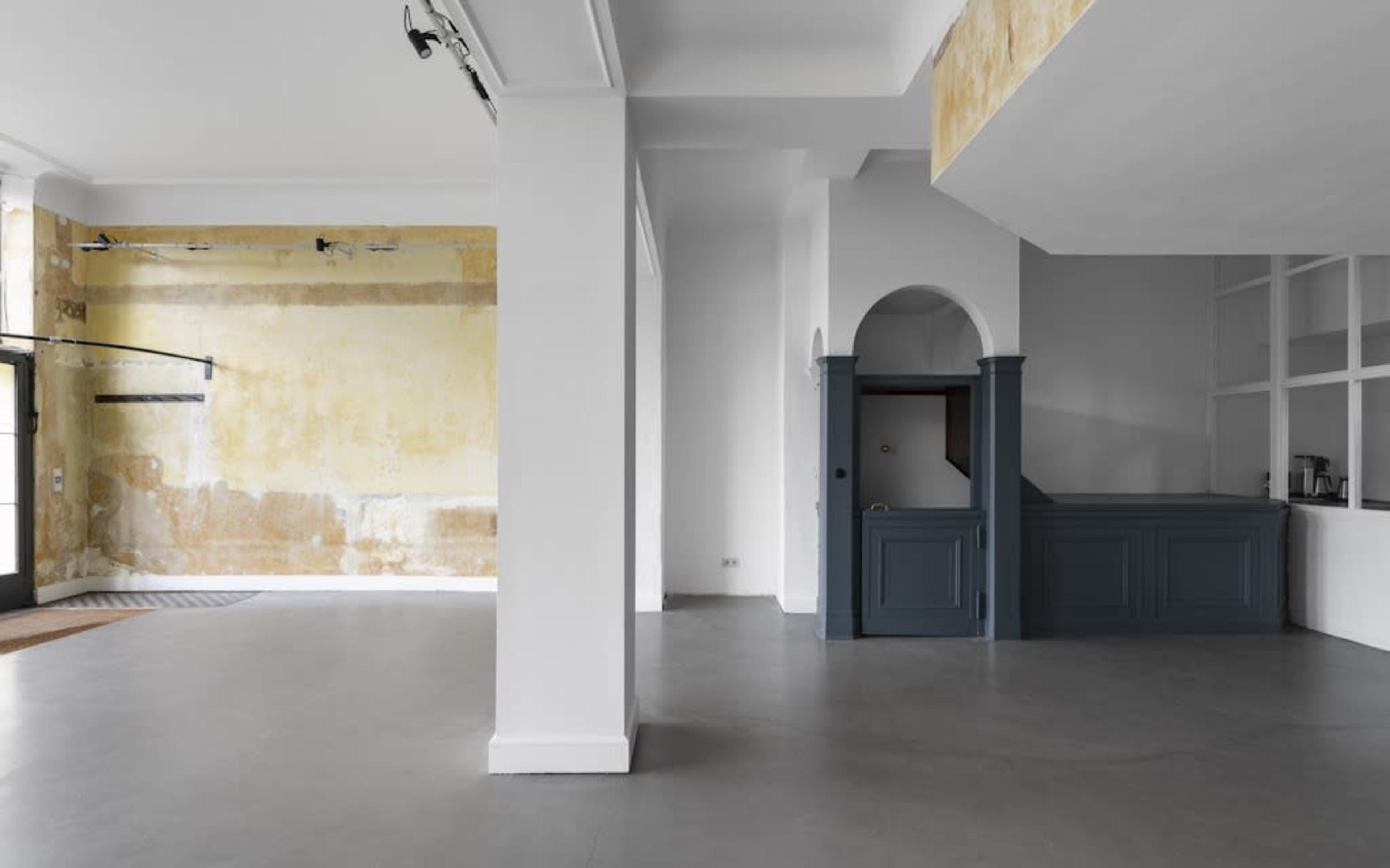 A spacious, empty room featuring a polished concrete floor, exposed walls with a mixture of textures, and a reception area with a dark blue counter.
