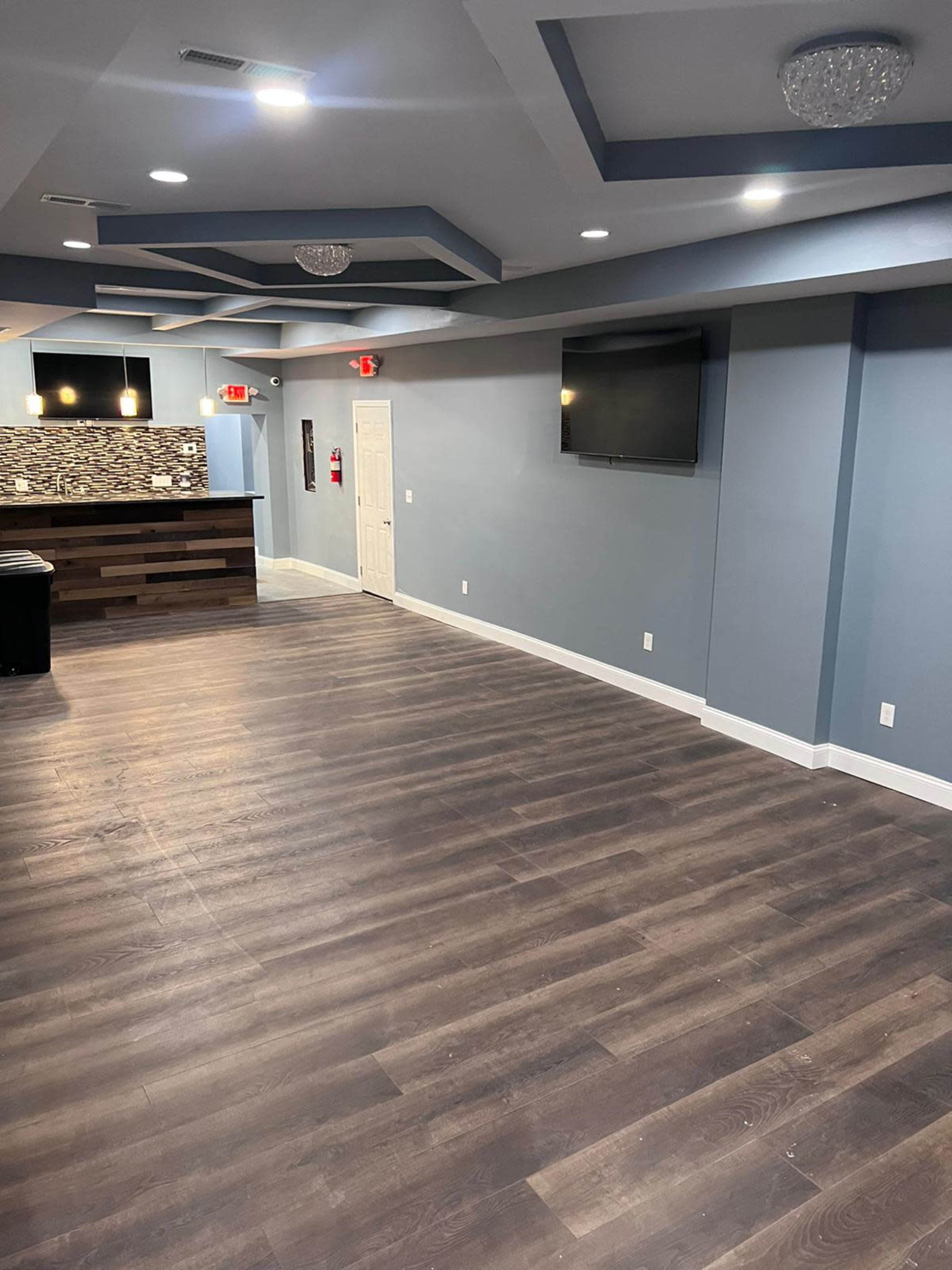 An empty interior space with hardwood flooring, a reception area featuring a counter, and blue-gray walls with recessed lighting.