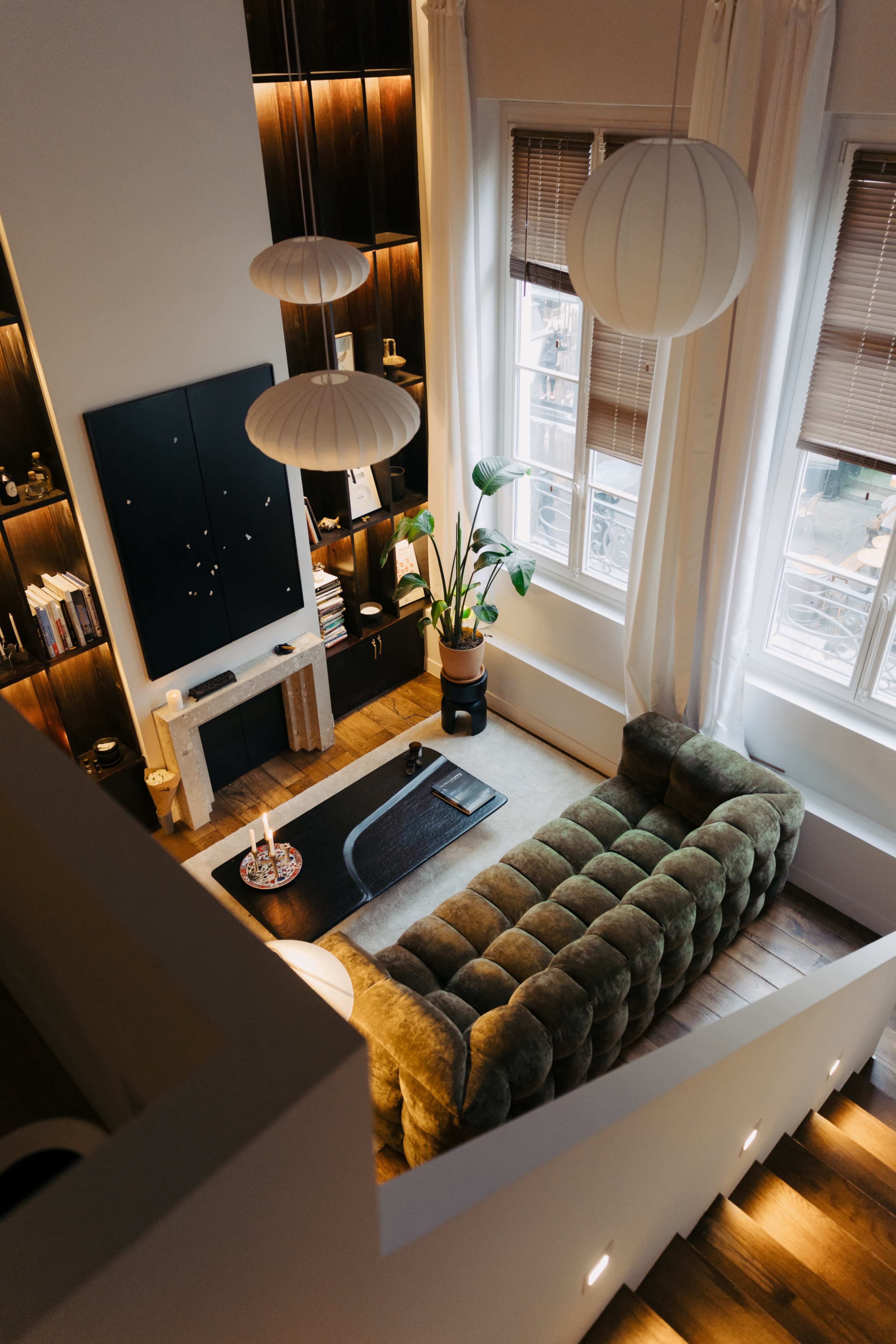 The image depicts a modern living room with a green tufted sofa, a coffee table, and decorative elements under stylish lighting fixtures.