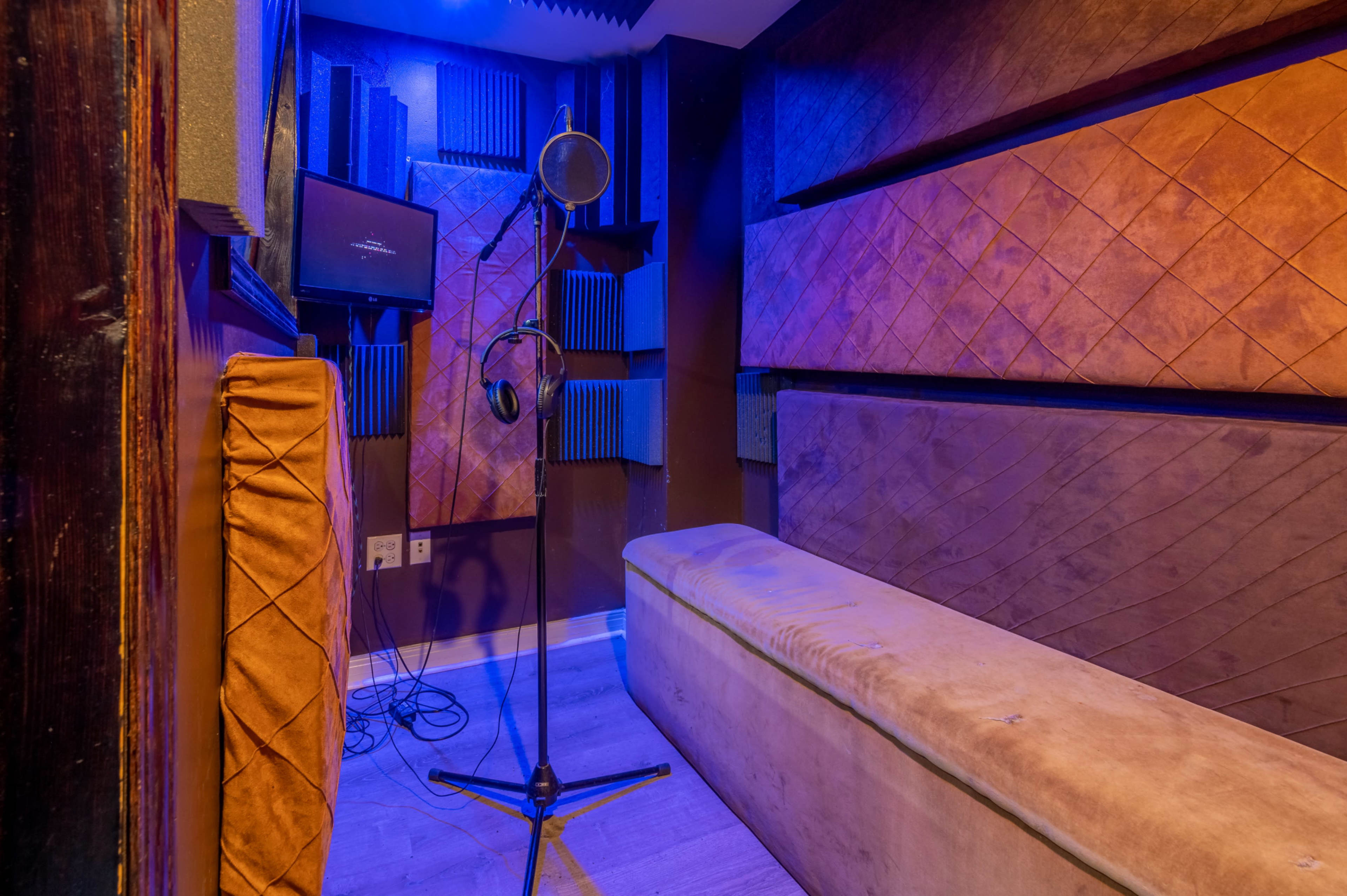 The image shows a small recording studio with a microphone on a stand, acoustic panels on the walls, and a cushioned bench.