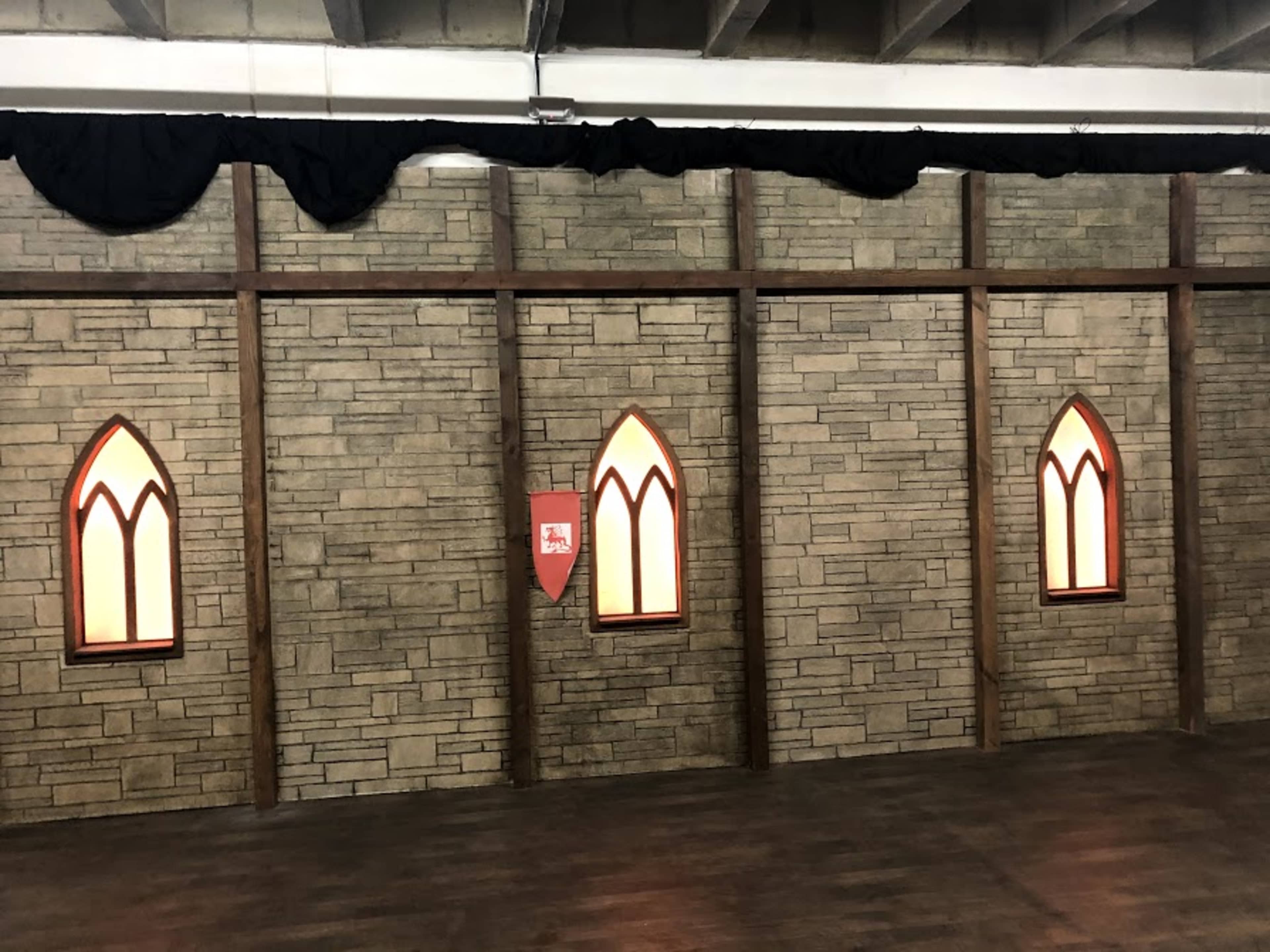 A textured stone wall with three arched windows and a red shield decoration.