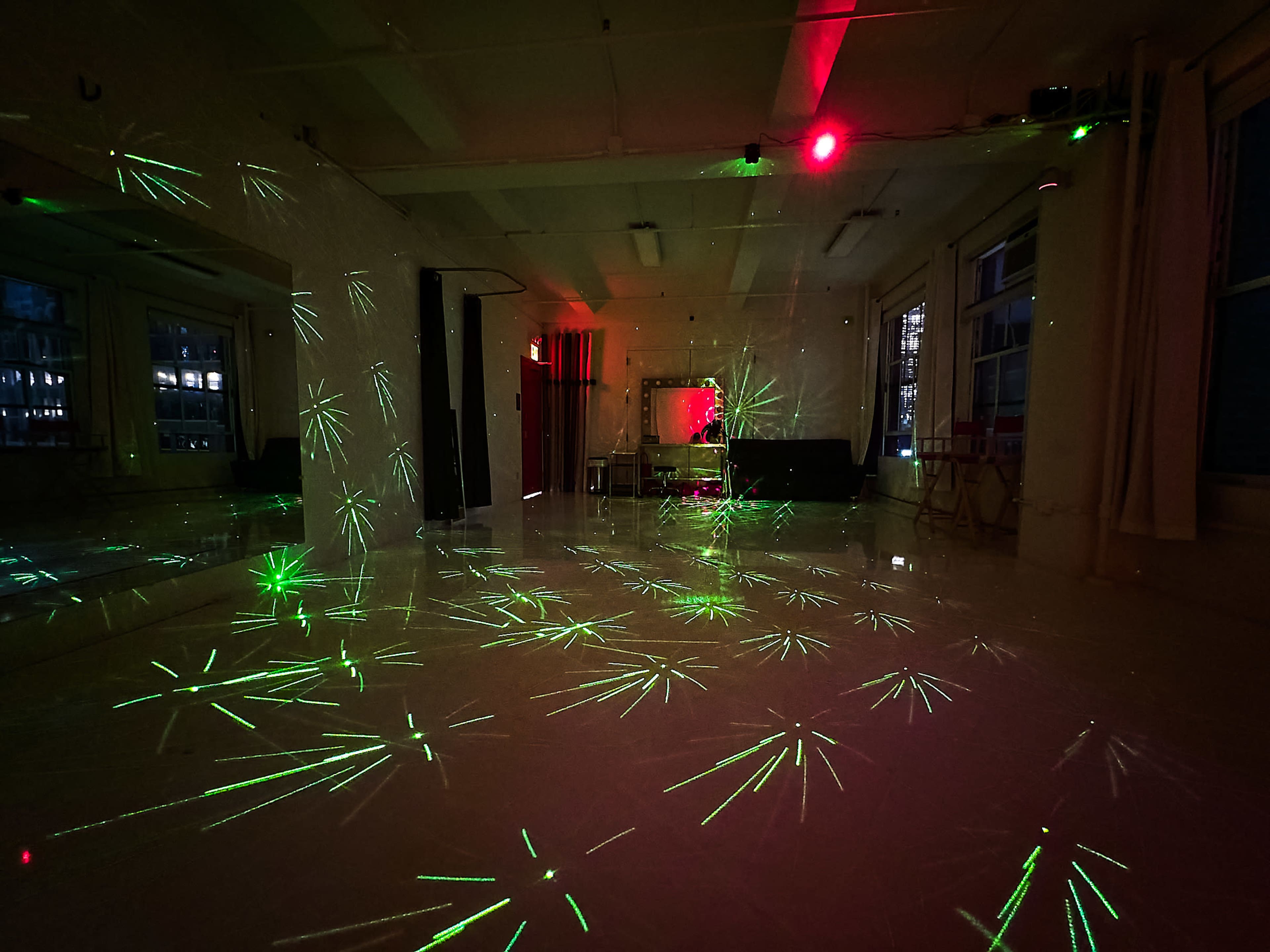 A dimly lit room with green and red laser lights projecting star-like patterns onto the white floor and walls.