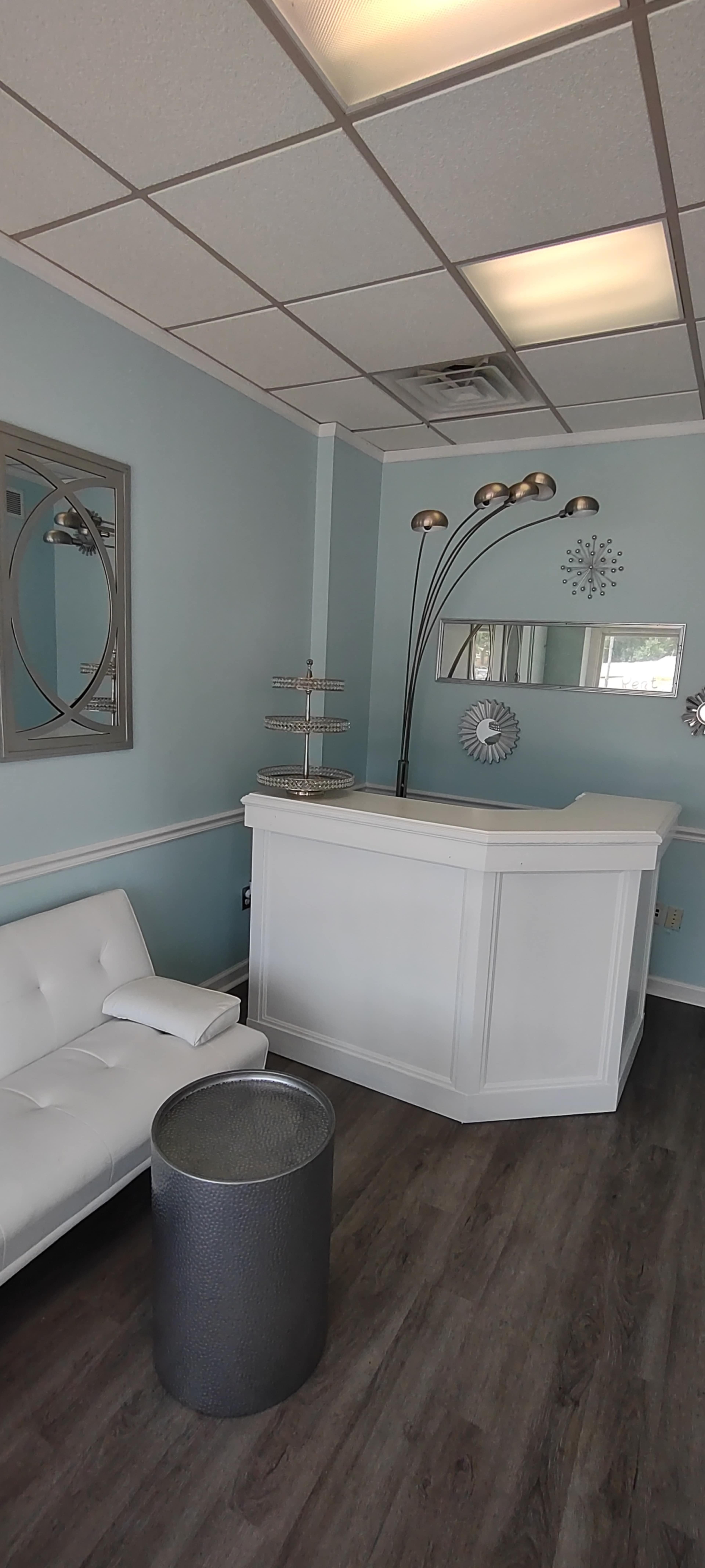 The image shows a waiting area with a white couch, a metallic side table, and a reception desk in a room with light blue walls and modern decor.