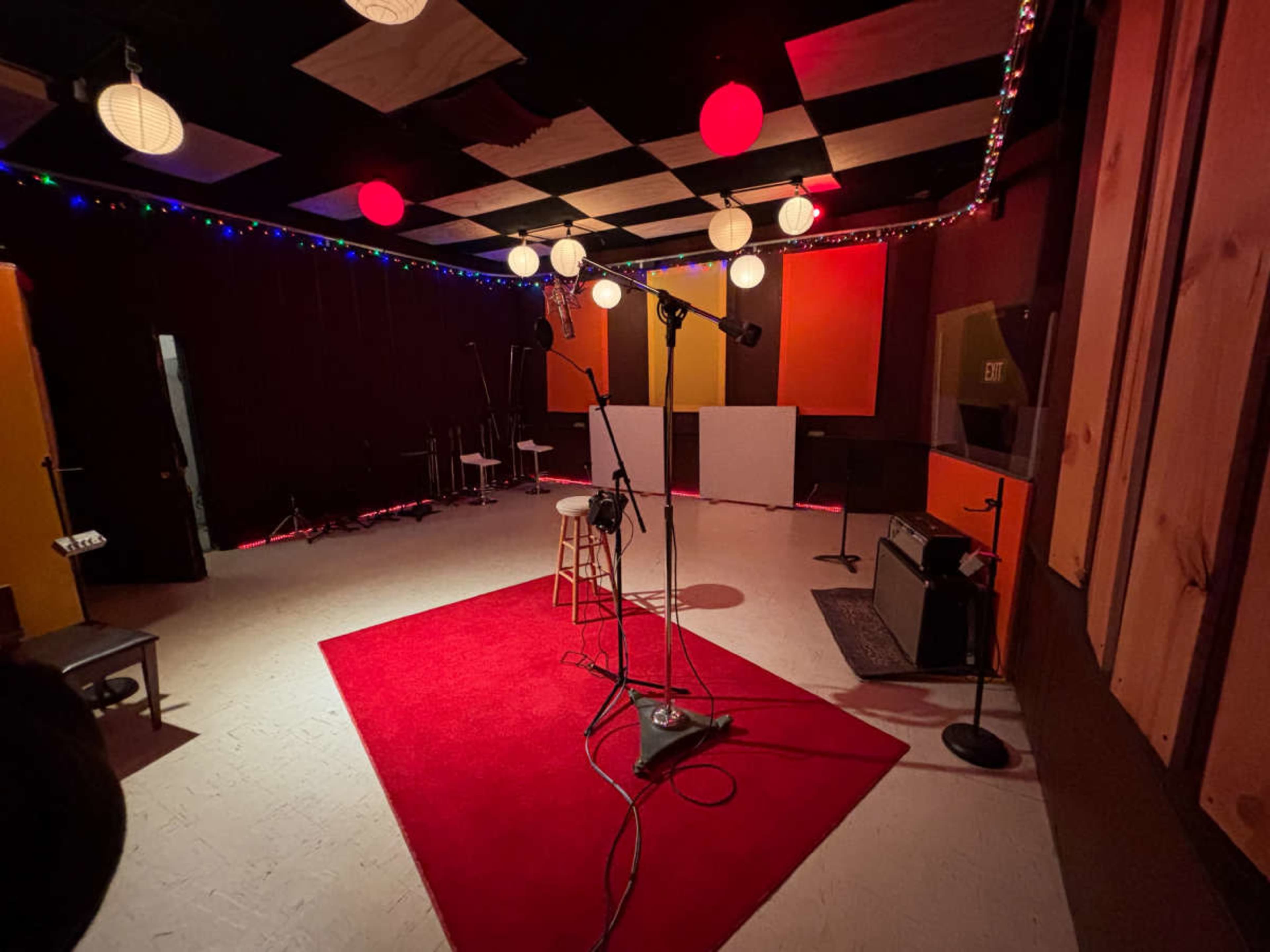 The image shows a music recording studio with red carpet, microphone stands, and colorful hanging lights.