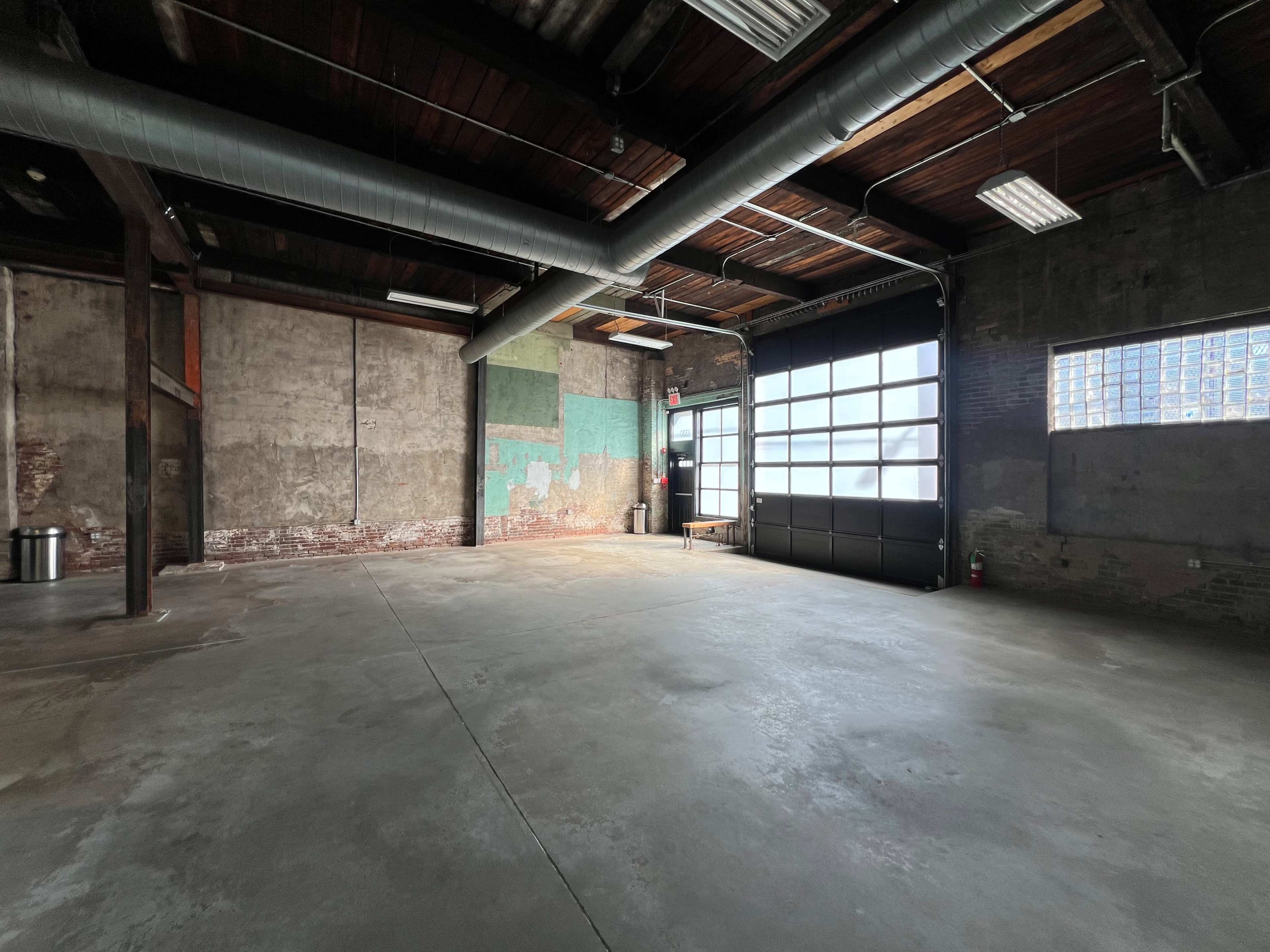 An empty industrial space with exposed brick walls, high ceilings, and large windows.