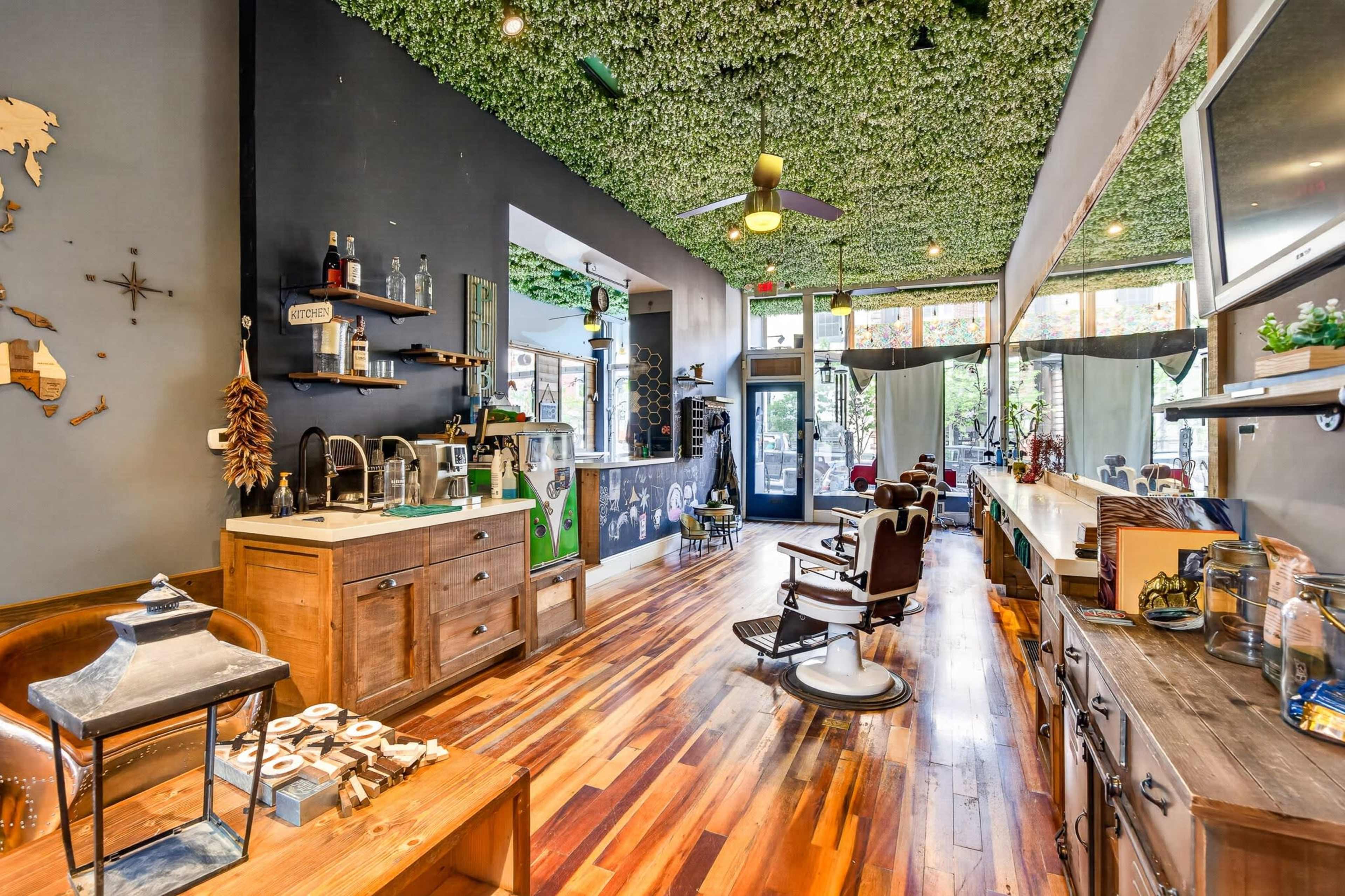 The image shows a stylish barbershop with wooden flooring, a green ceiling, and vintage barber chairs.