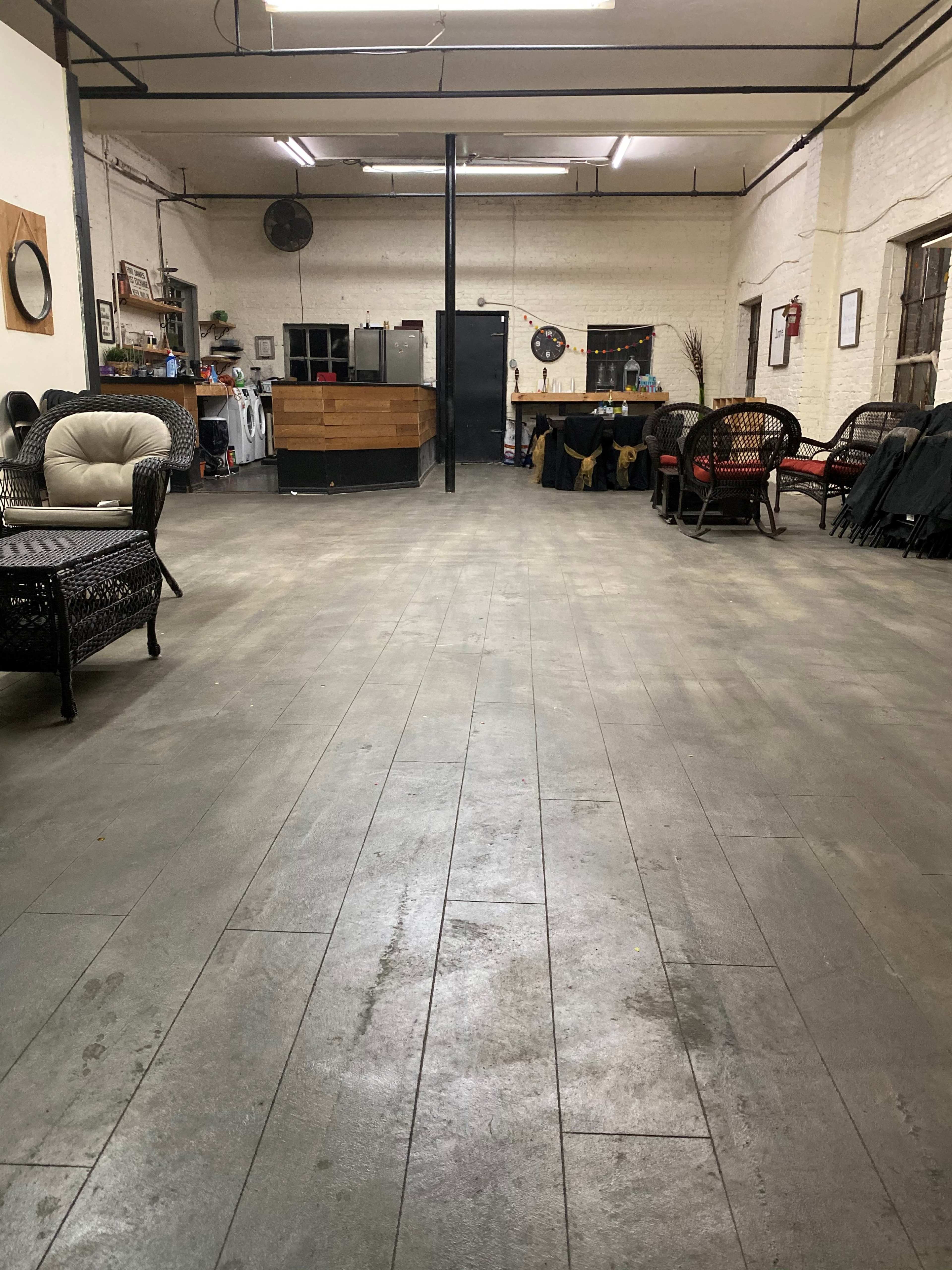 An empty, spacious room with wooden flooring, featuring chairs along the sides and a wooden counter at the far end.