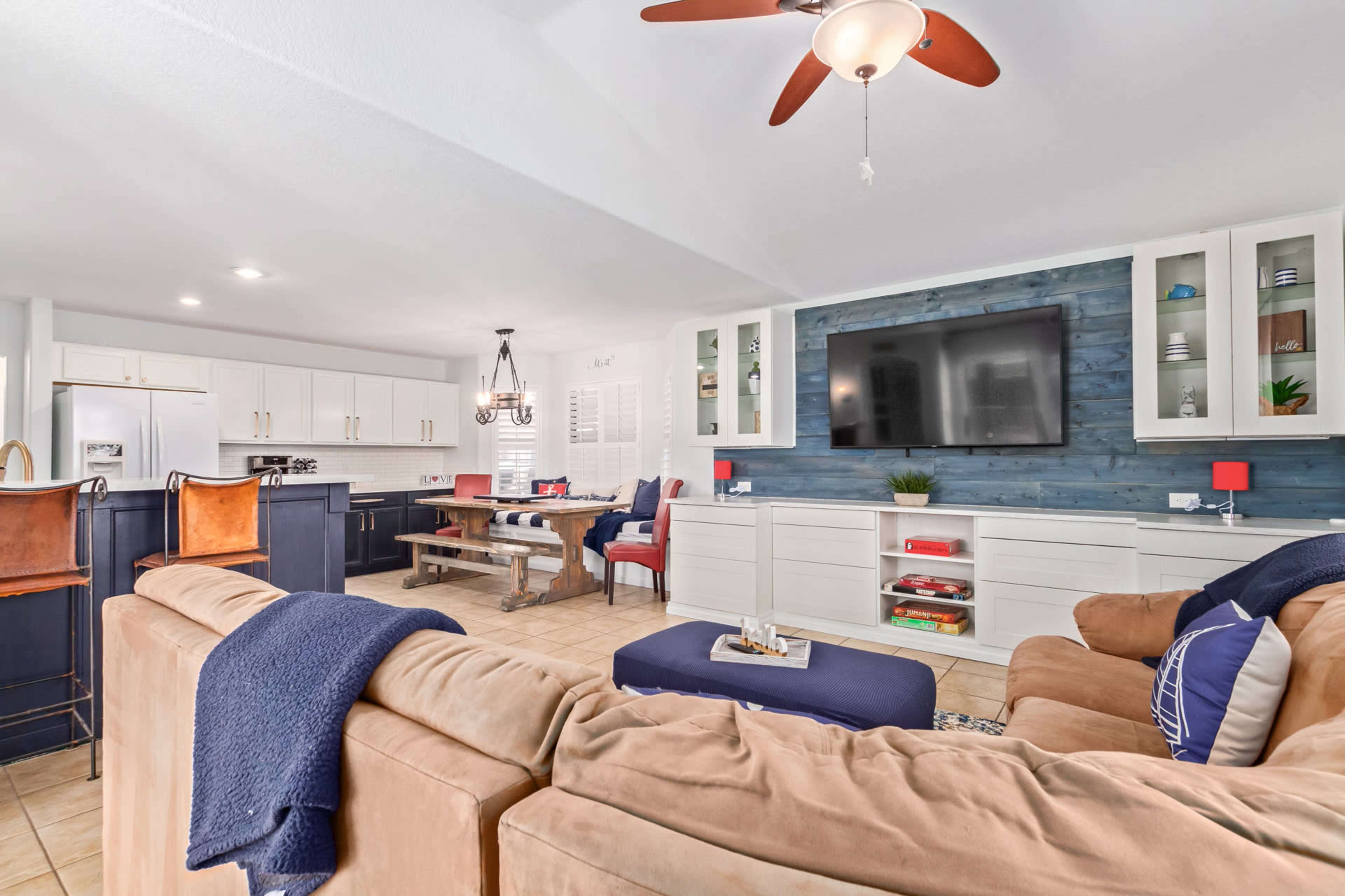 The image shows a modern living room with a tan sectional sofa, a blue ottoman, and a large television mounted on a blue accent wall.