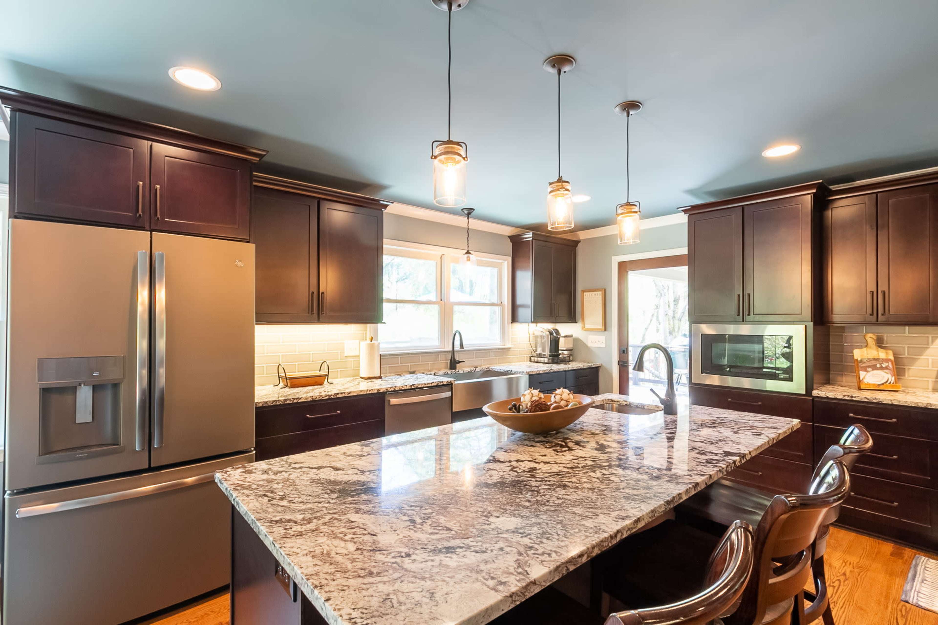 The kitchen features dark cabinetry, a large granite island, and pendant lighting over the dining area.