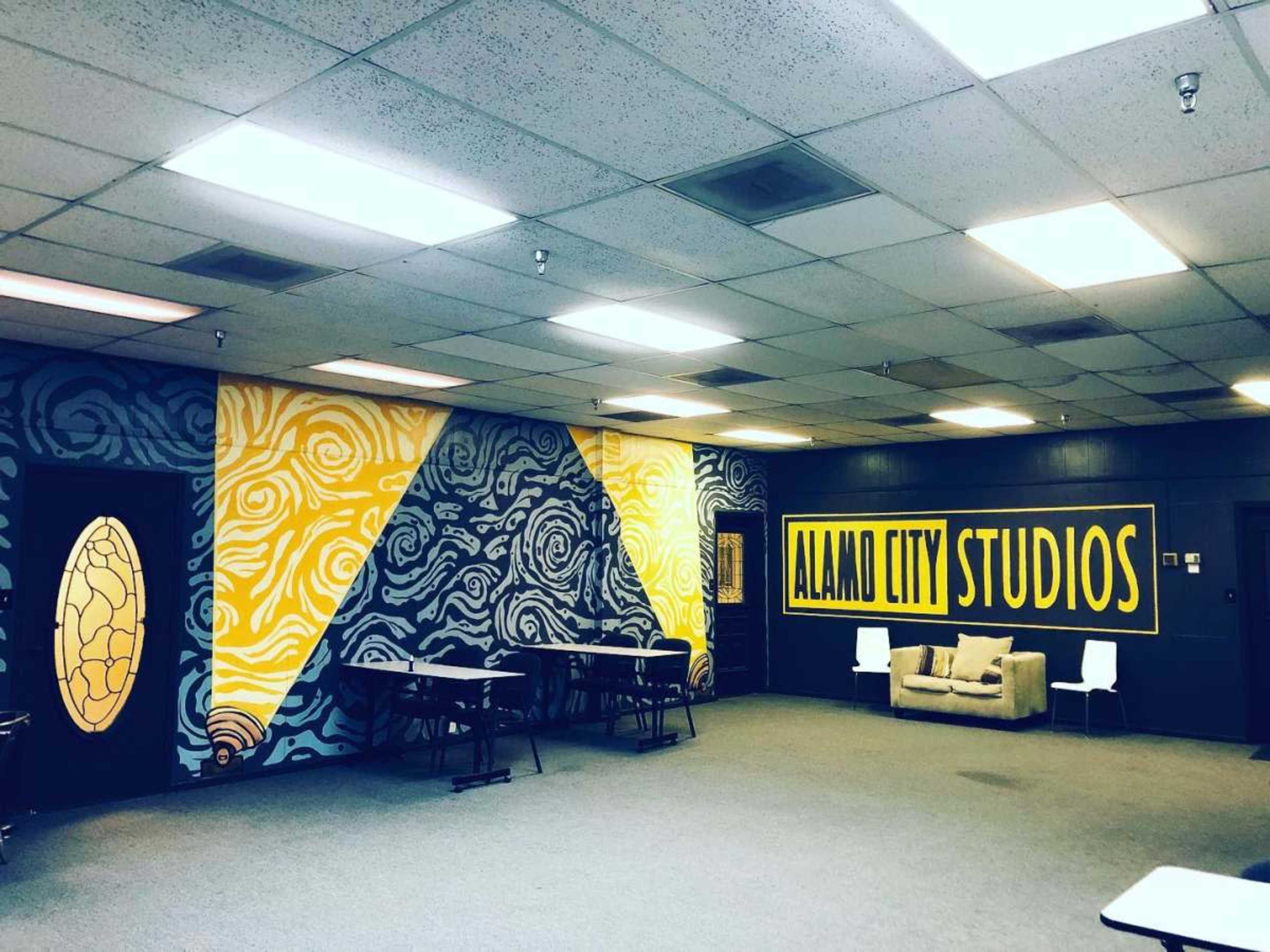 The image shows a spacious studio room with colorful wall murals, tables, and a couch.