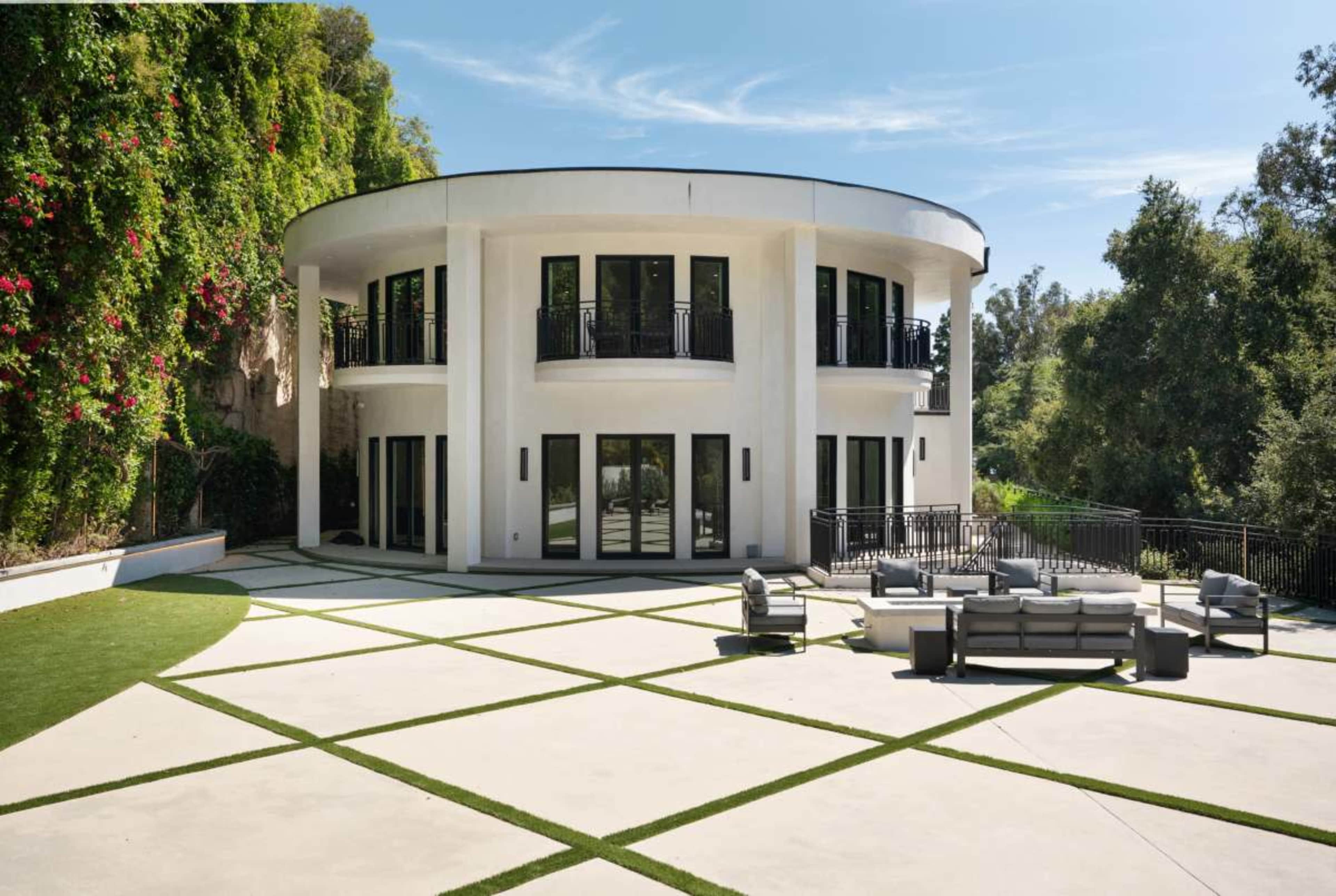 The image shows a modern, circular building with large windows and an extensive patio area featuring geometric landscaping.