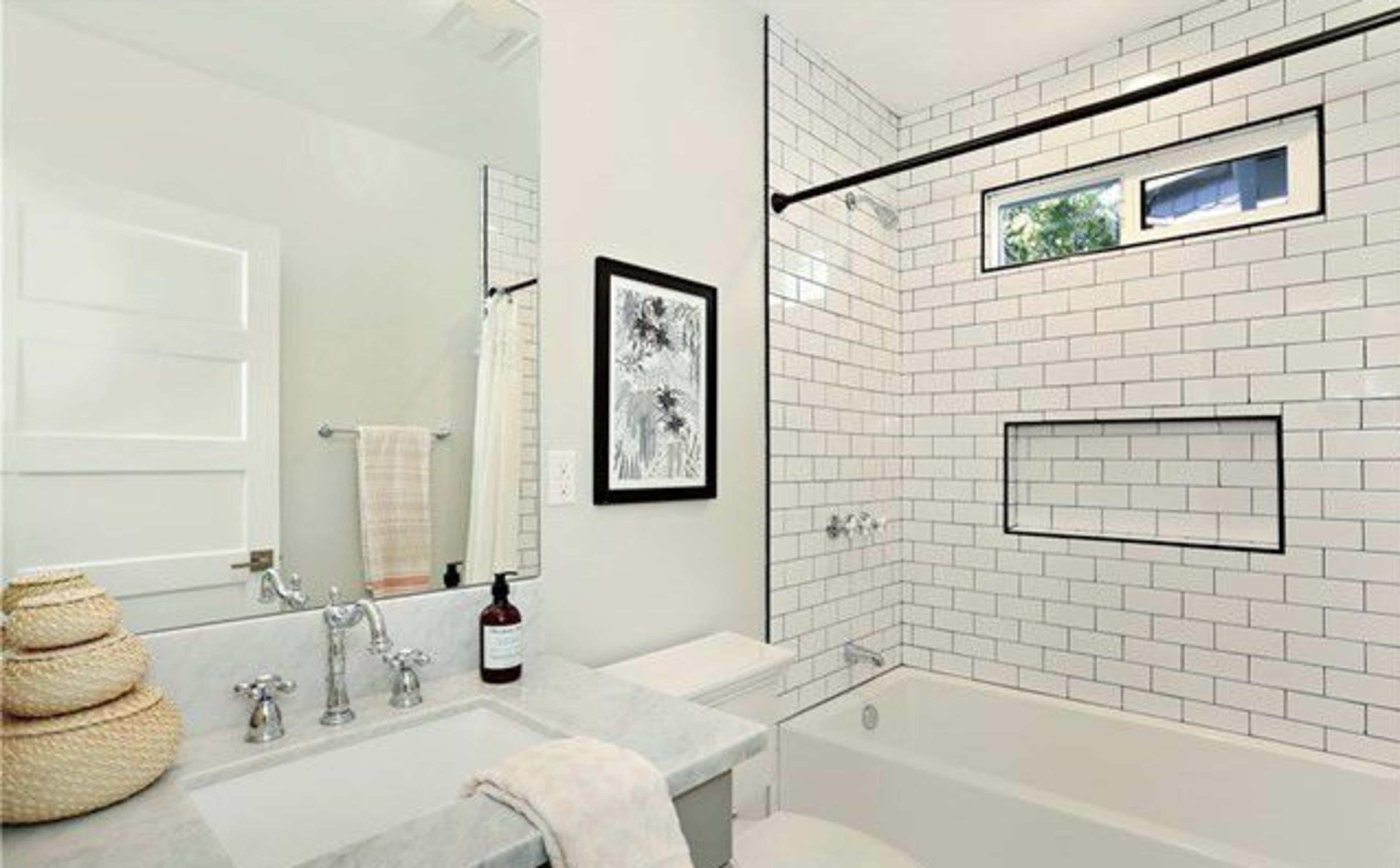 The bathroom features white tiled walls, a combination bathtub and shower, a marble countertop sink, and a window above the bathtub.