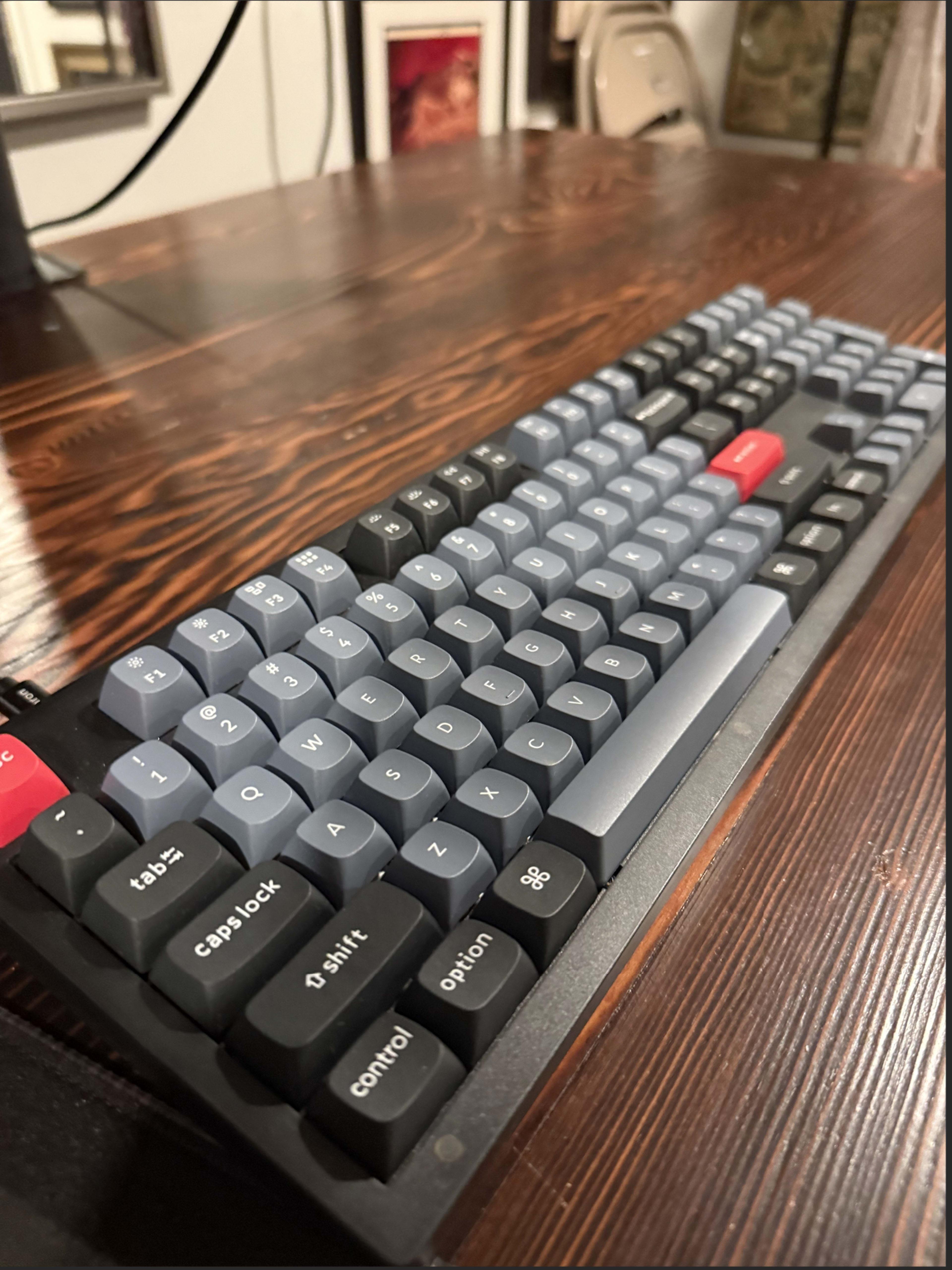 The image shows a mechanical keyboard with a gray and black color scheme resting on a wooden table.