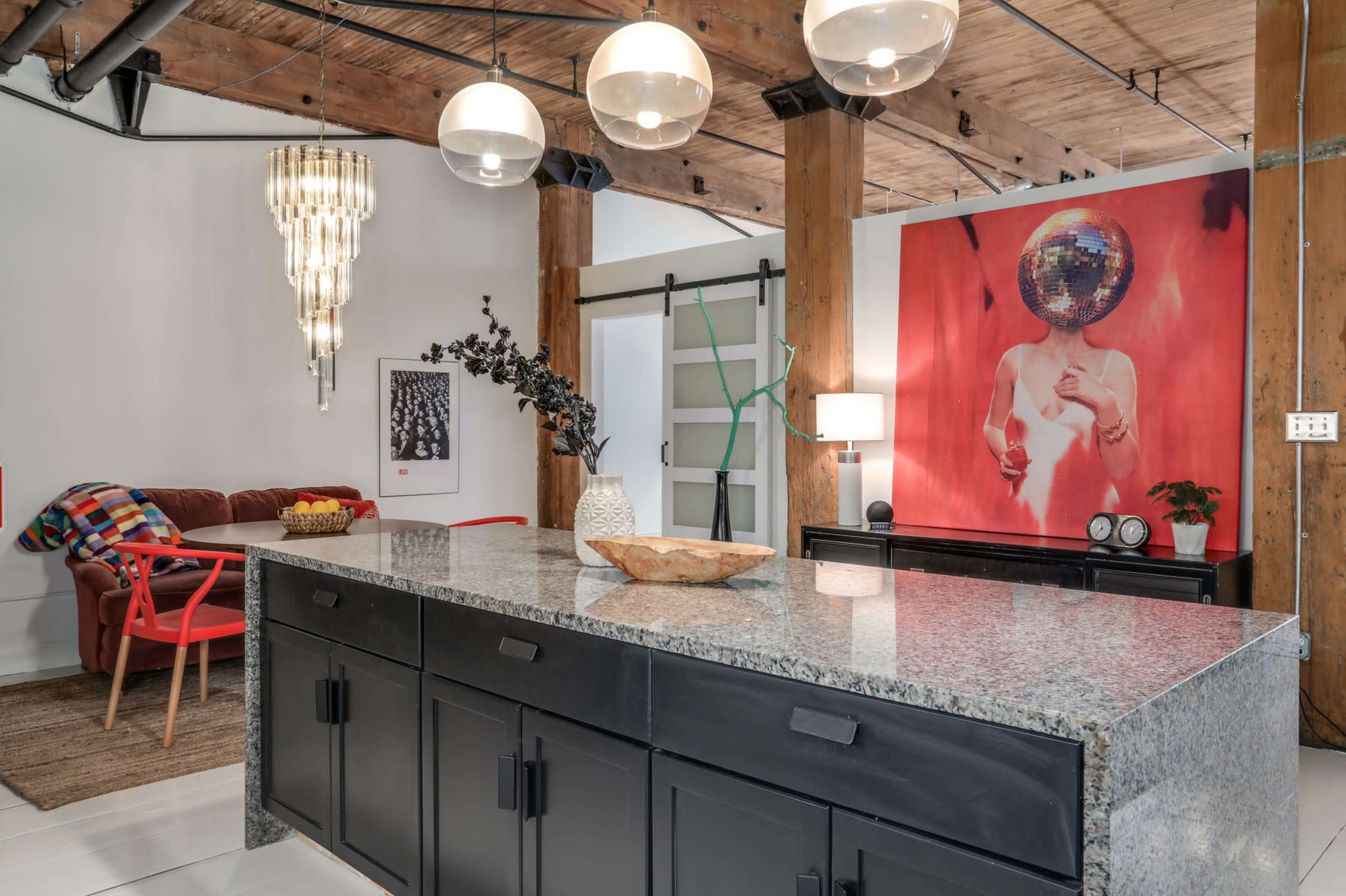 A modern kitchen with a large granite island, pendant lighting, and a vibrant artwork featuring a disco ball on the wall.