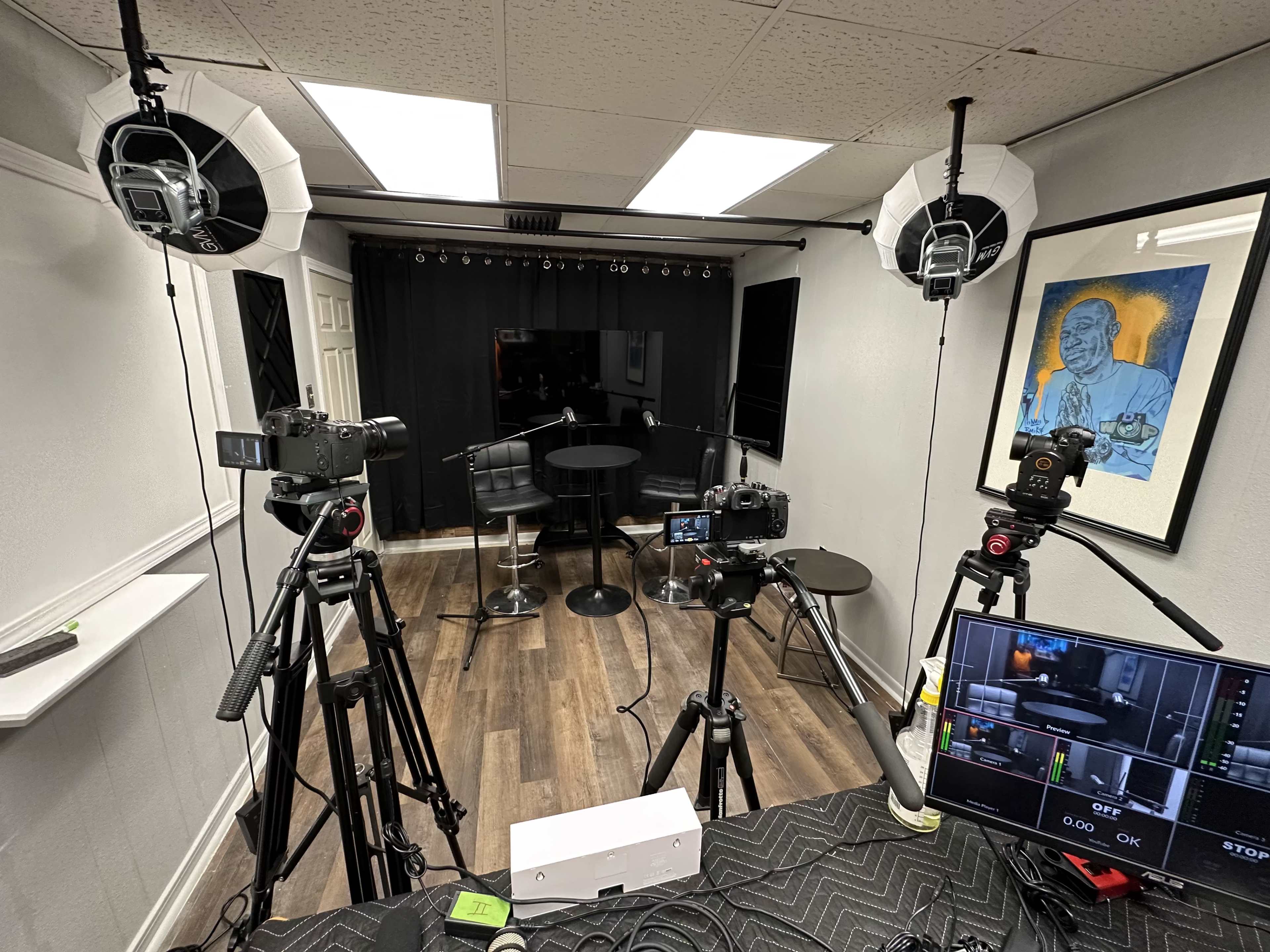 The image shows a filming setup with multiple cameras and lighting equipment arranged around a small black table in a studio space.