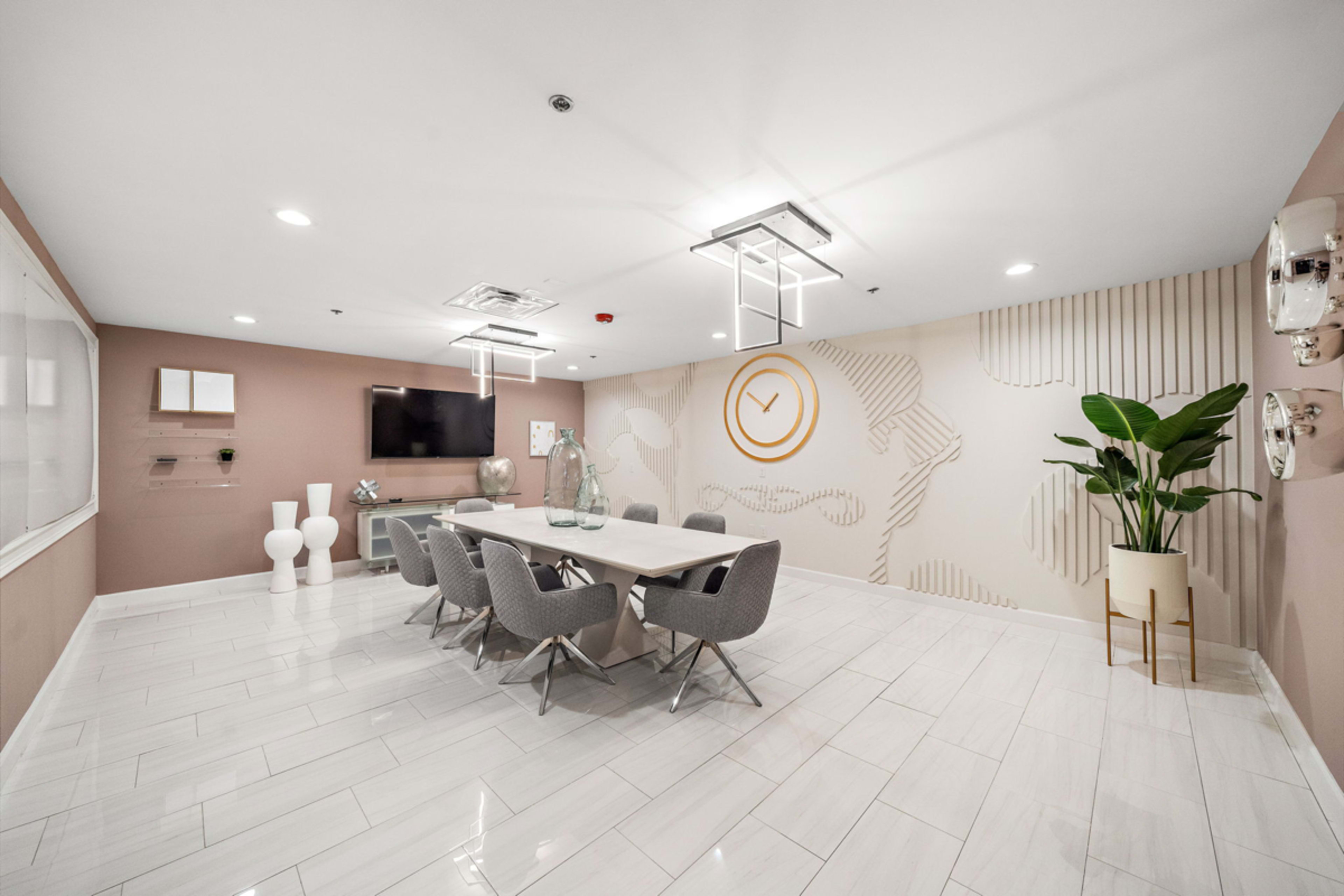 A modern meeting room with a long table surrounded by chairs, a television mounted on the wall, and a large plant in the corner.