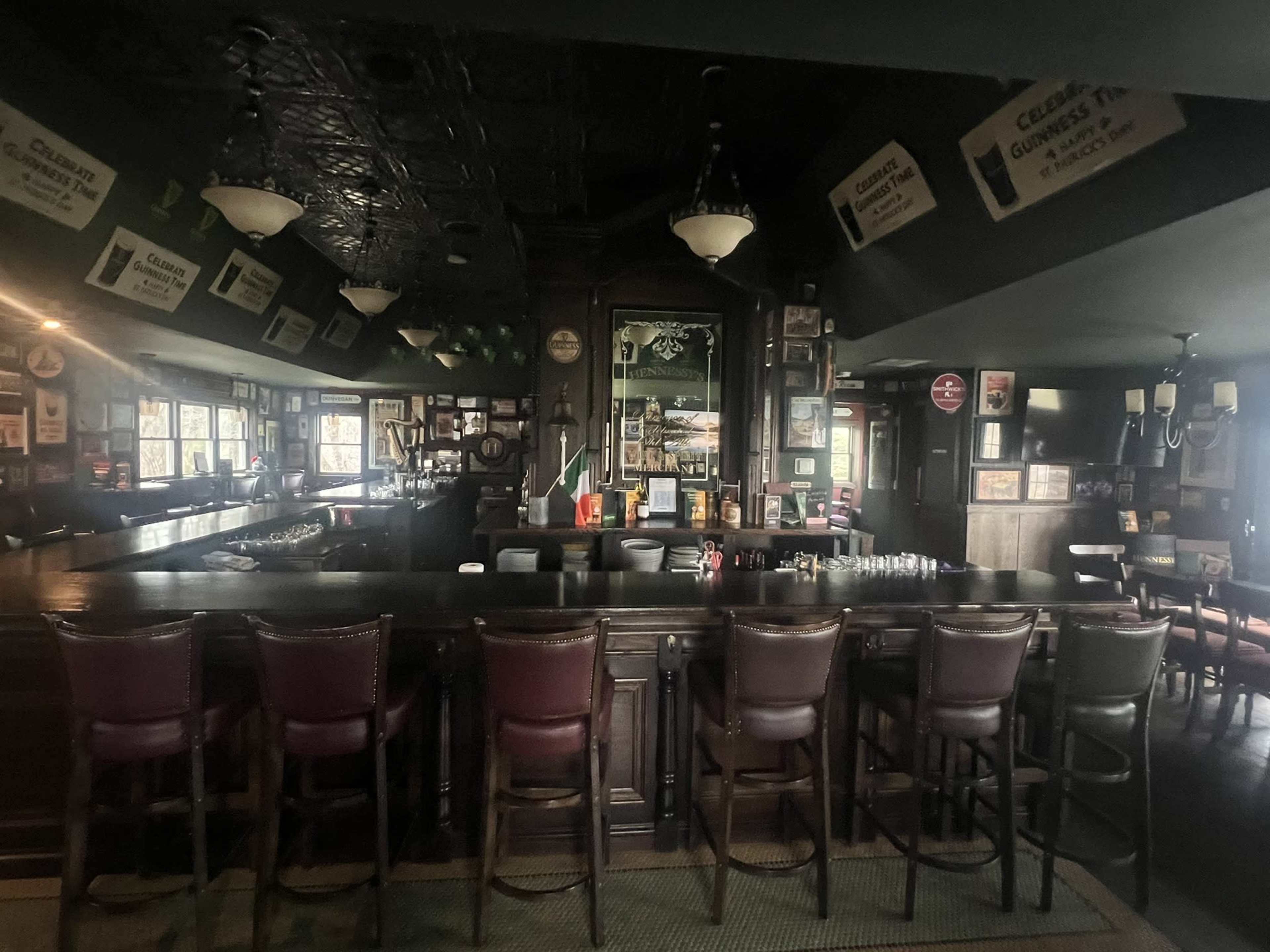 The image shows an empty pub with a wooden bar, high-backed stools, and vintage decor on the walls.