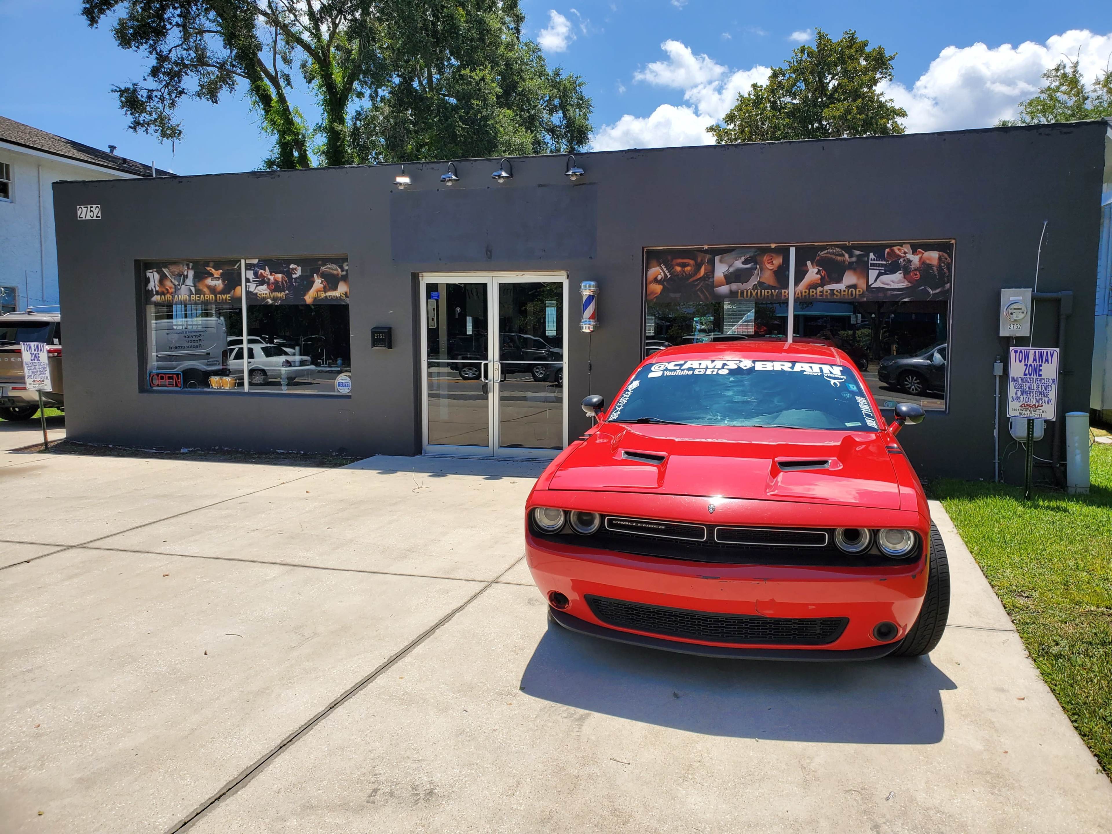 A bright red car is parked in front of a gray building with large windows displaying various promotional posters.