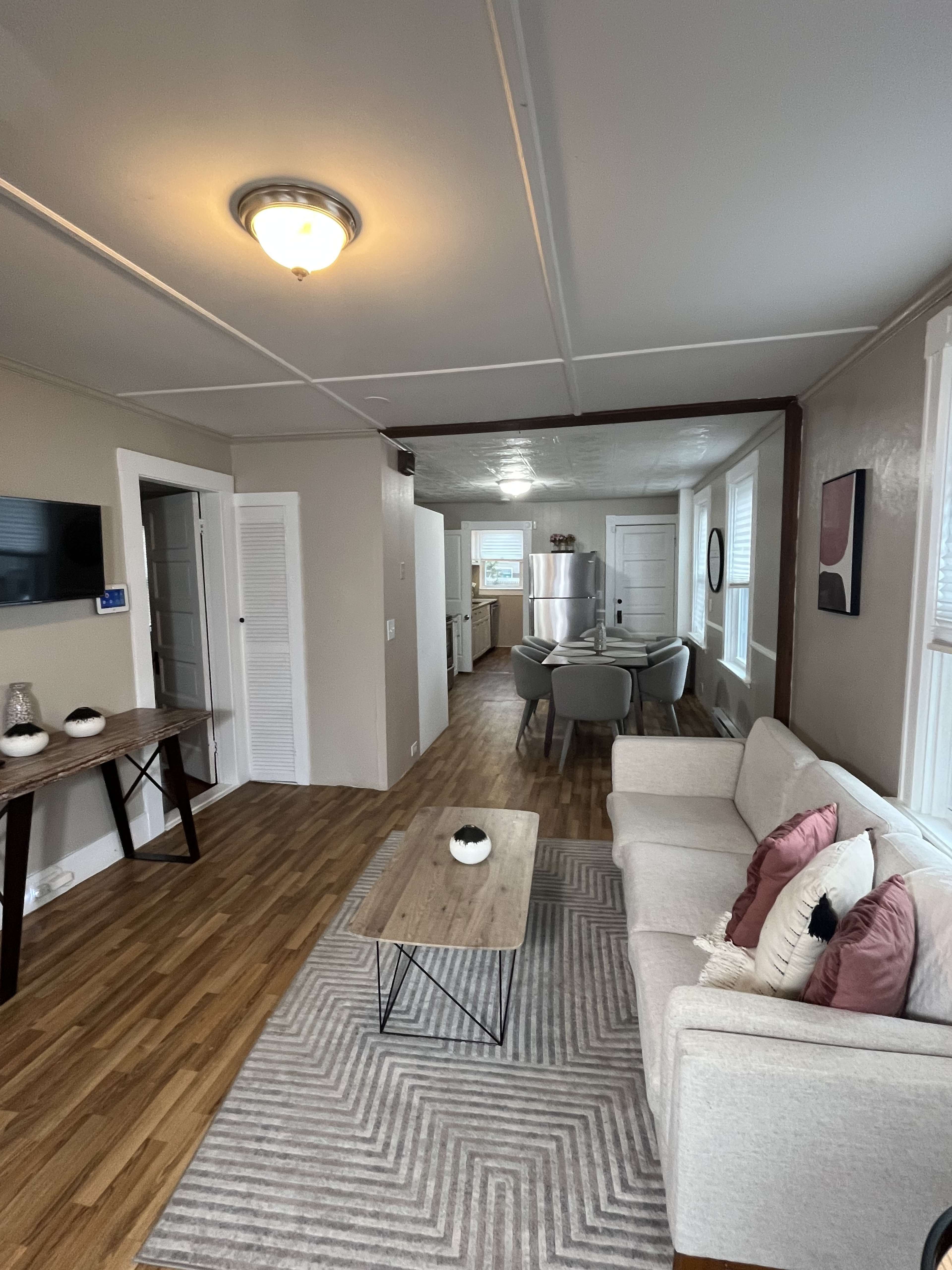 The image shows a living space with a light-colored sofa, a coffee table, and a dining area visible in the background.
