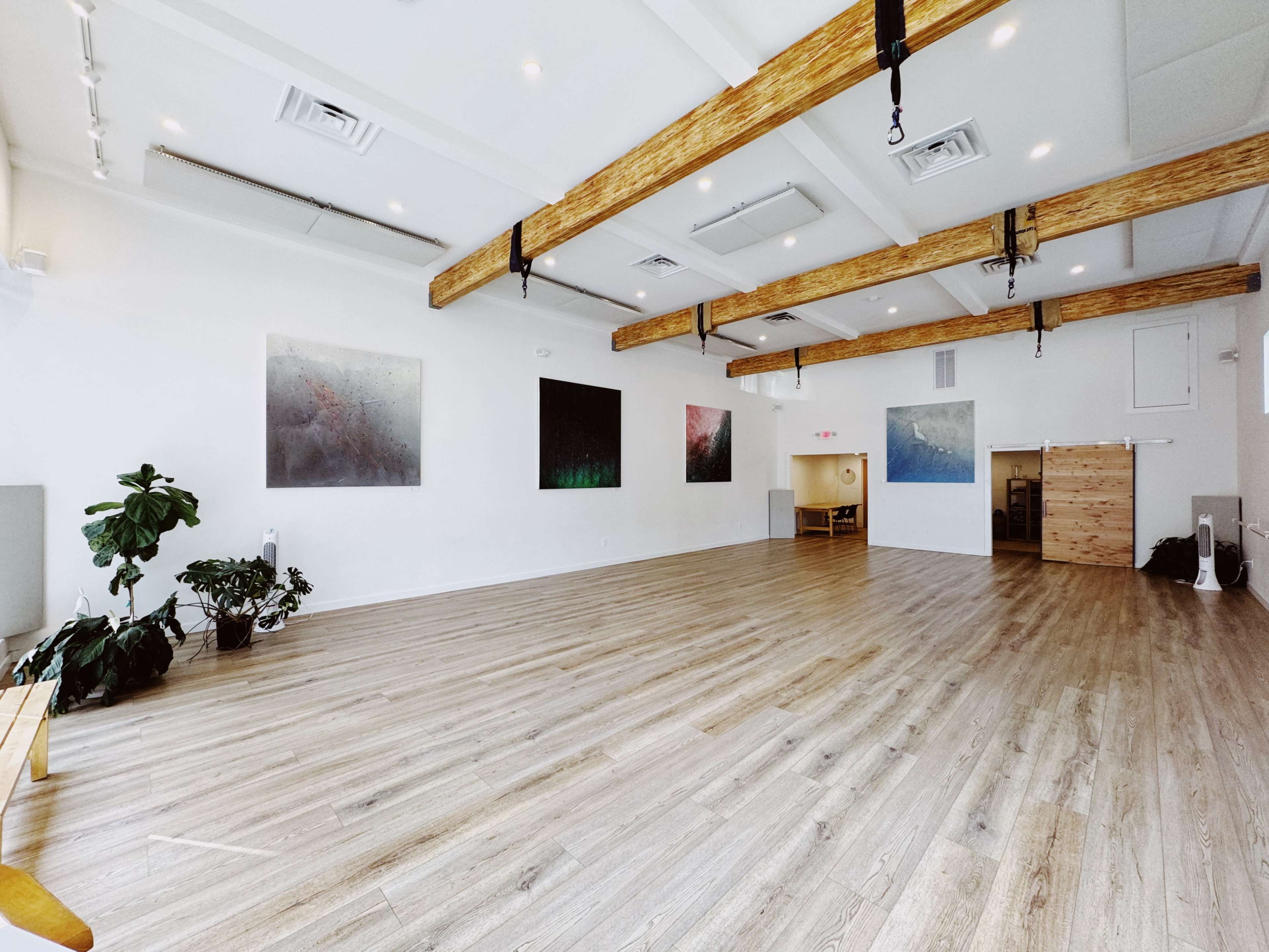 A spacious, well-lit room with wooden beams and large abstract paintings on the walls.