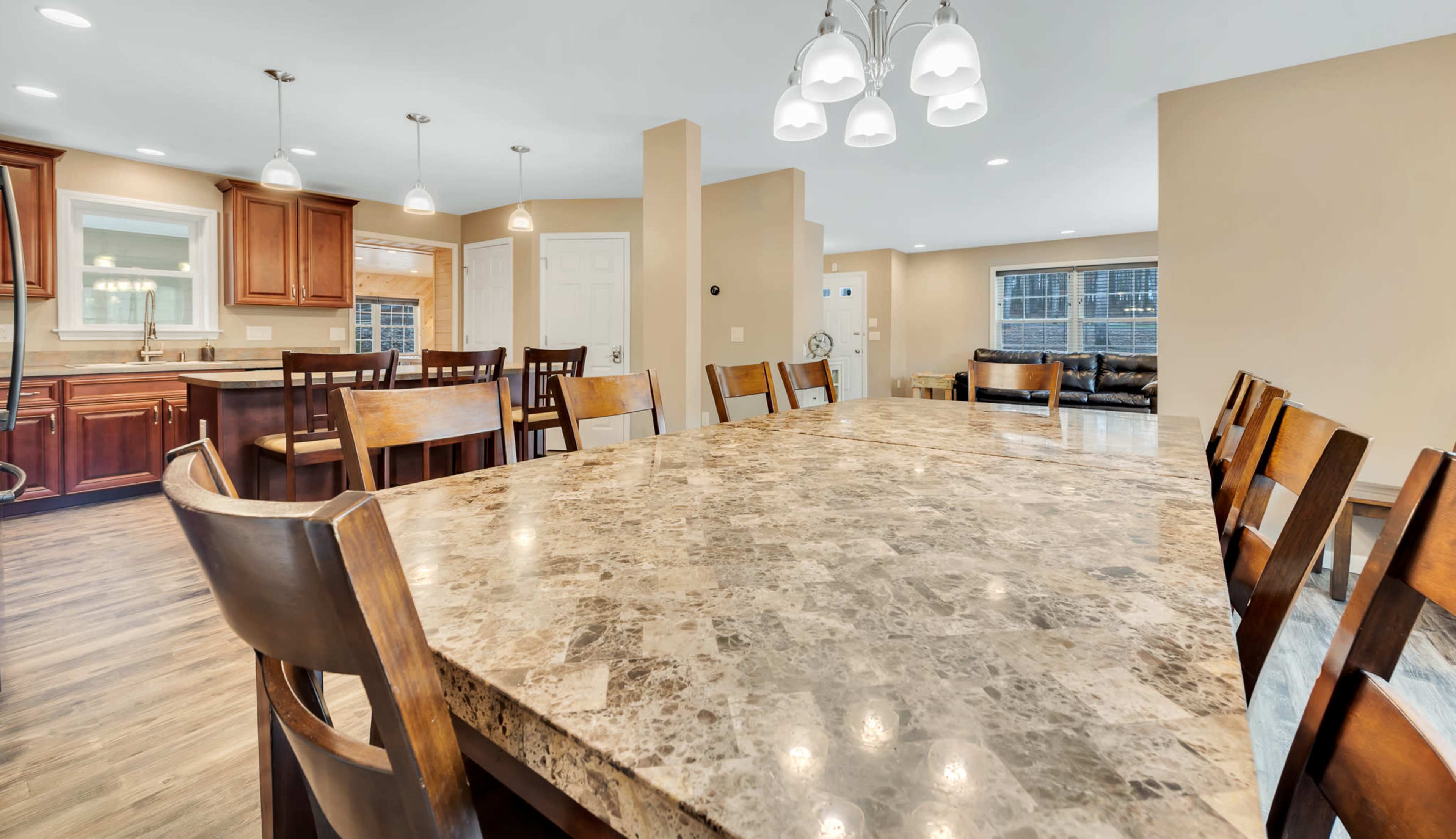 A large dining table with wooden chairs is positioned in a spacious kitchen area, adjacent to a living space with a sofa.