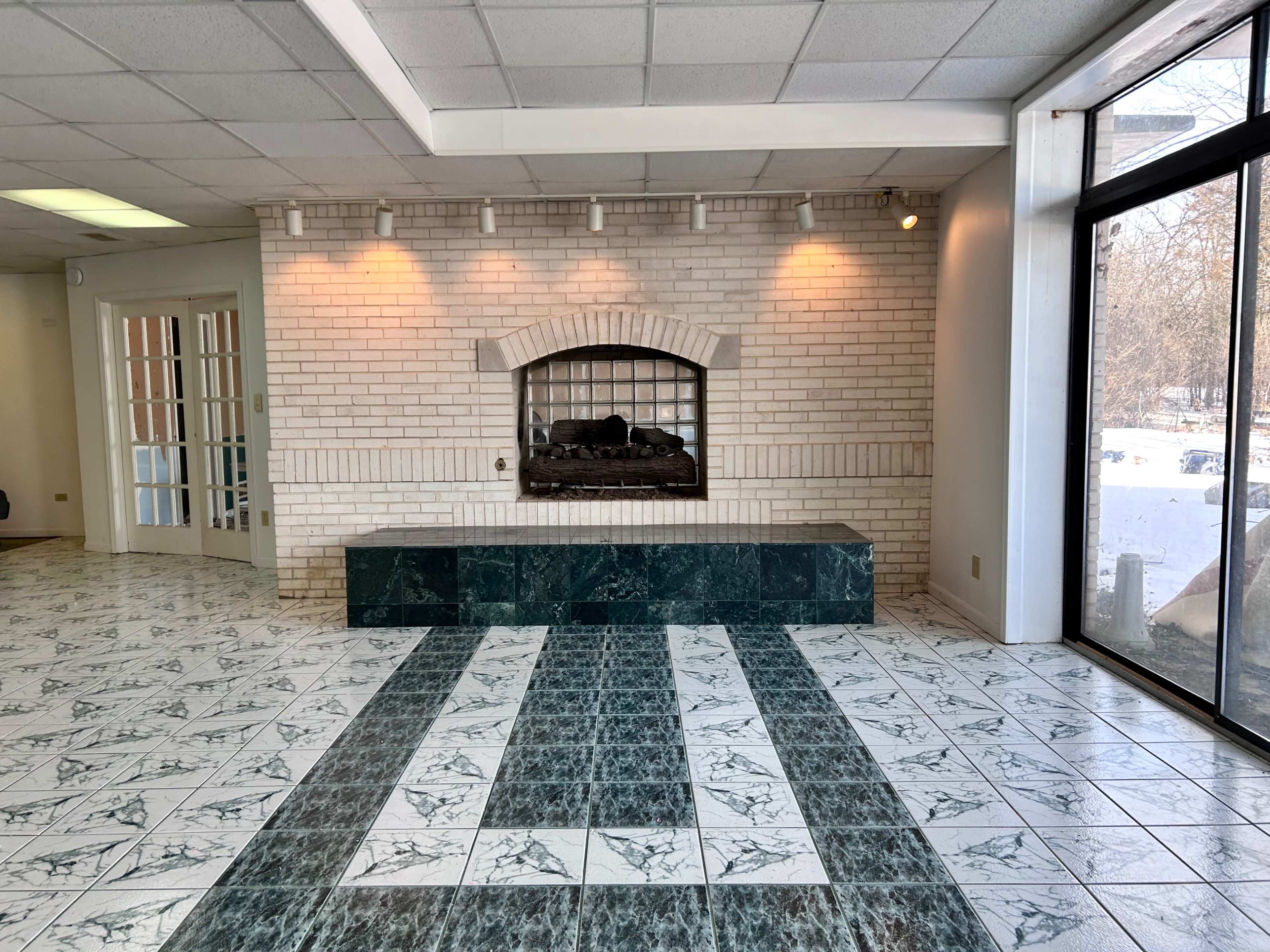 The image shows a spacious lobby area featuring a brick fireplace with a dark green marble base and a patterned tiled floor.