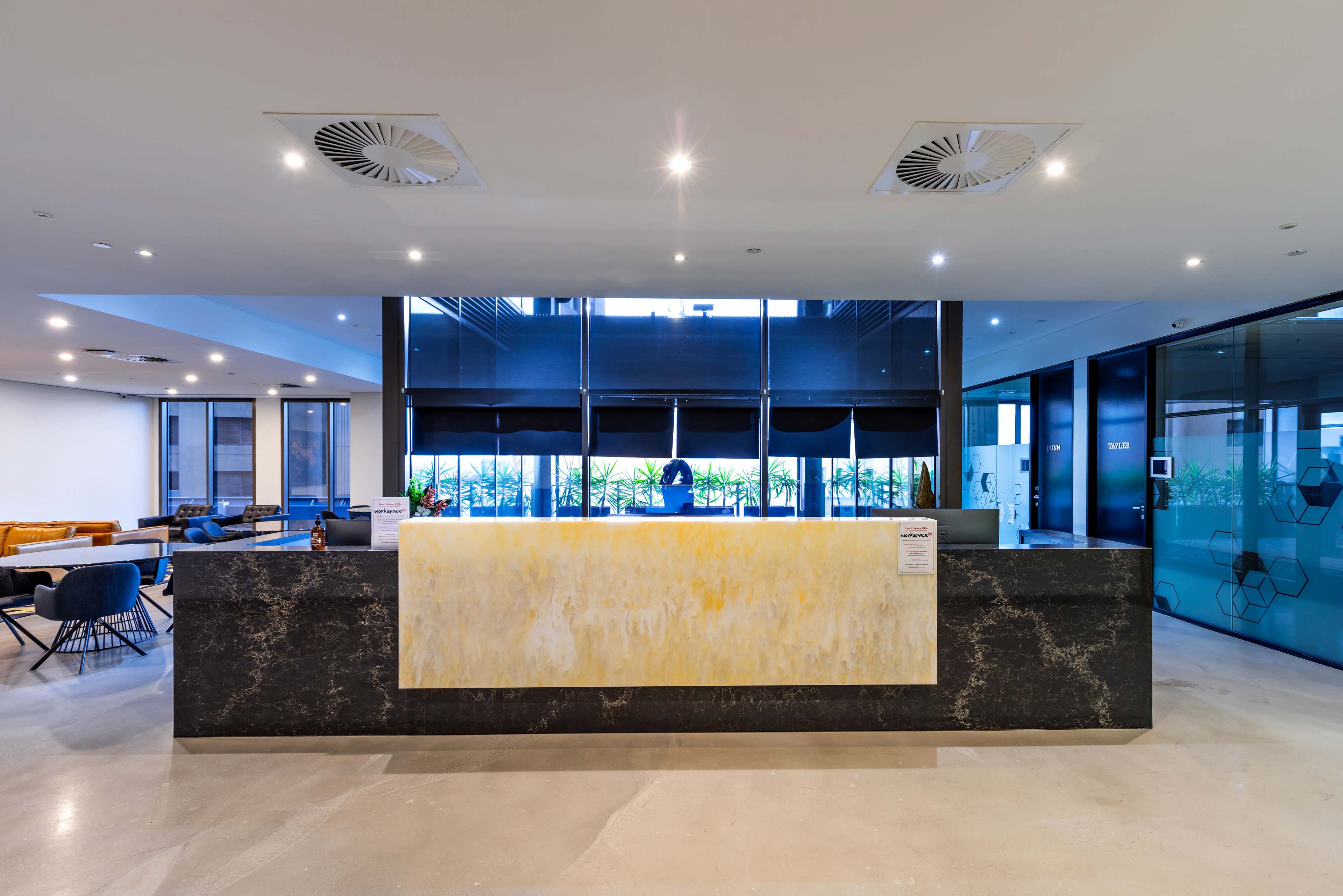 The image shows a modern reception area featuring a large, backlit onyx reception desk against a backdrop of glass walls and contemporary furnishings.