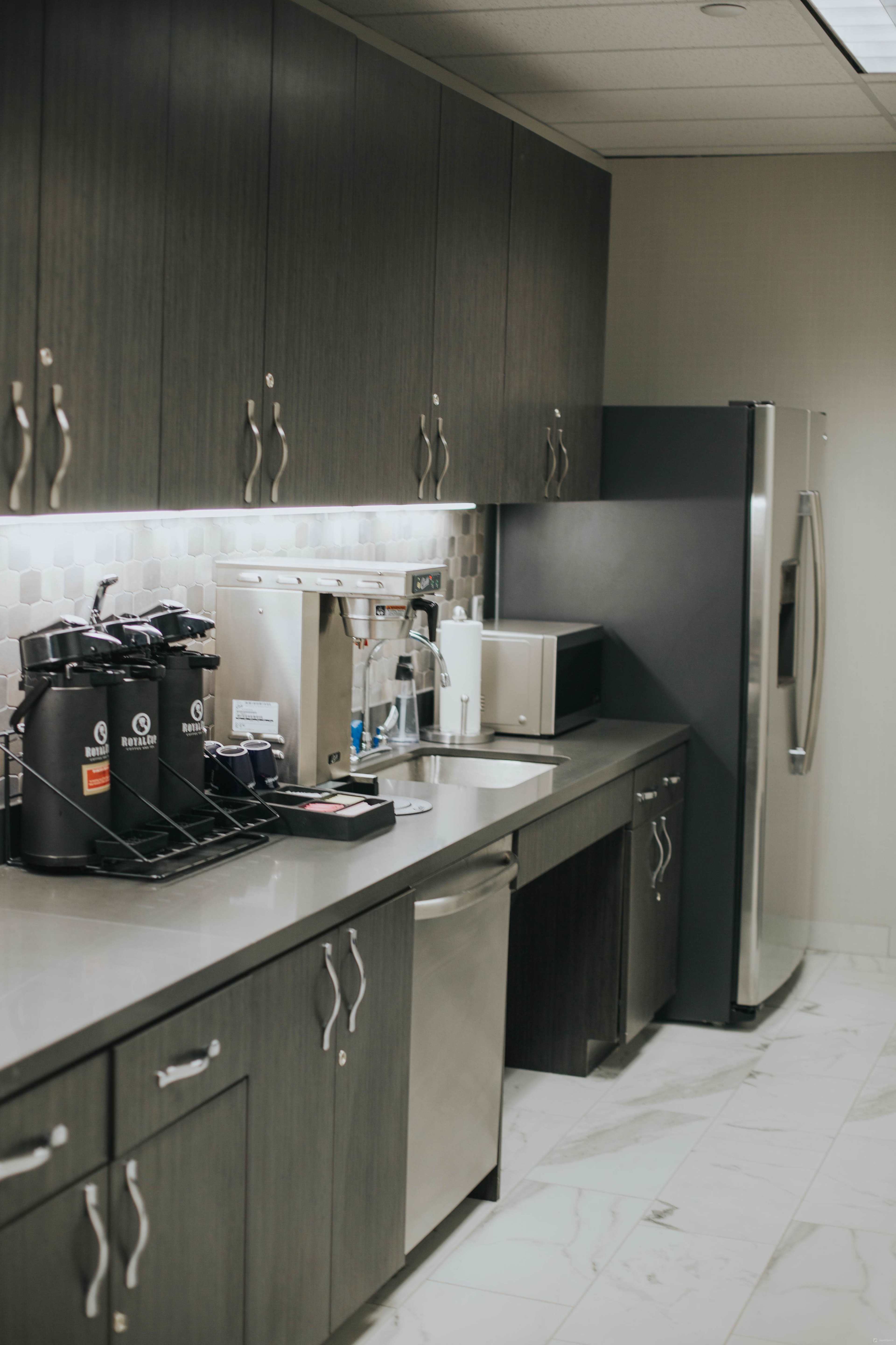A modern kitchen area features a gray countertop, a refrigerator, a microwave, a coffee maker, and a dishwasher, with sleek cabinetry above.